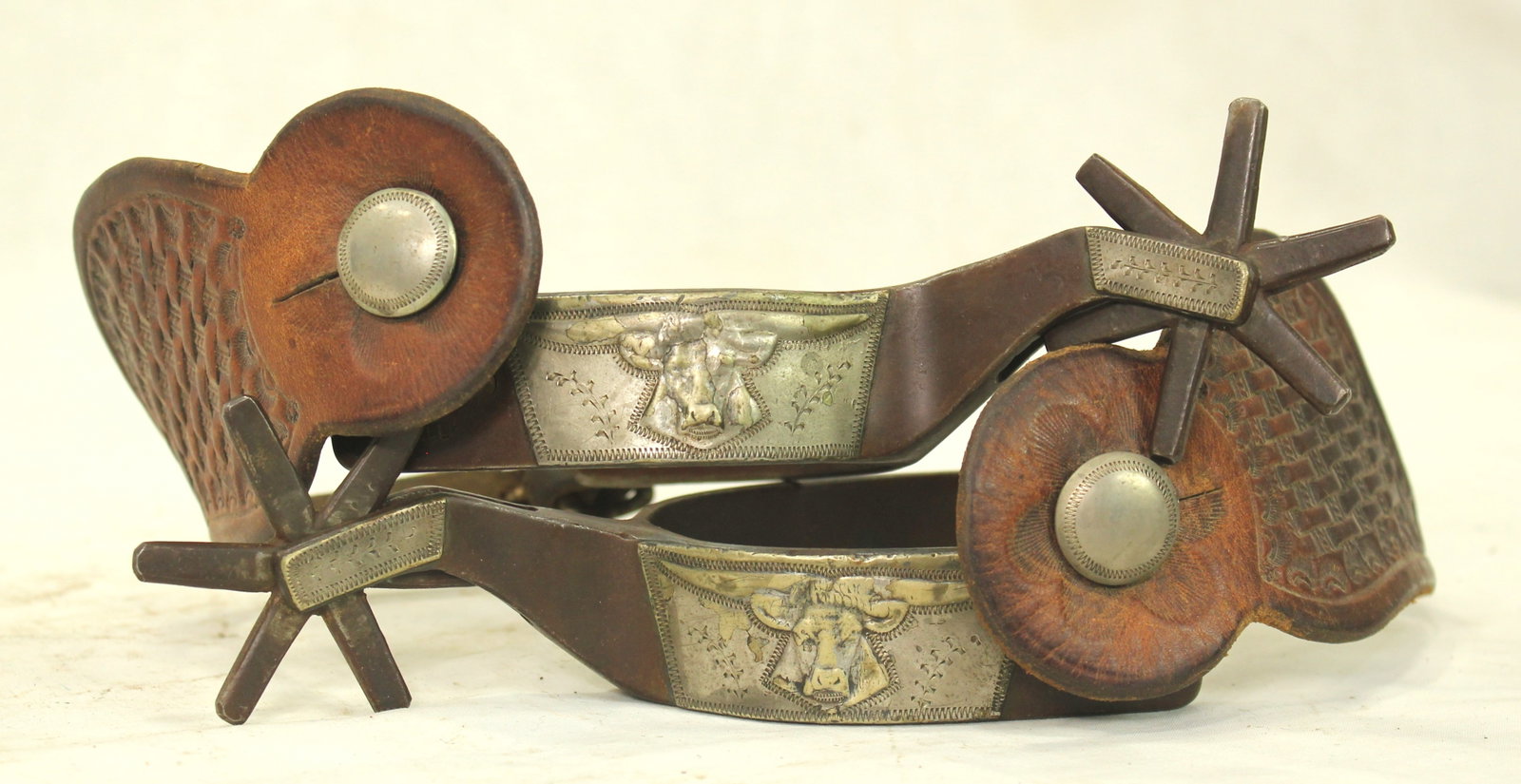 Kelly Bullhead Spurs: A great looking pair of single mounted spurs, silver mounted with three- dimensional steerheads, swinging buttons, huge 6-point rowels, and original straps.