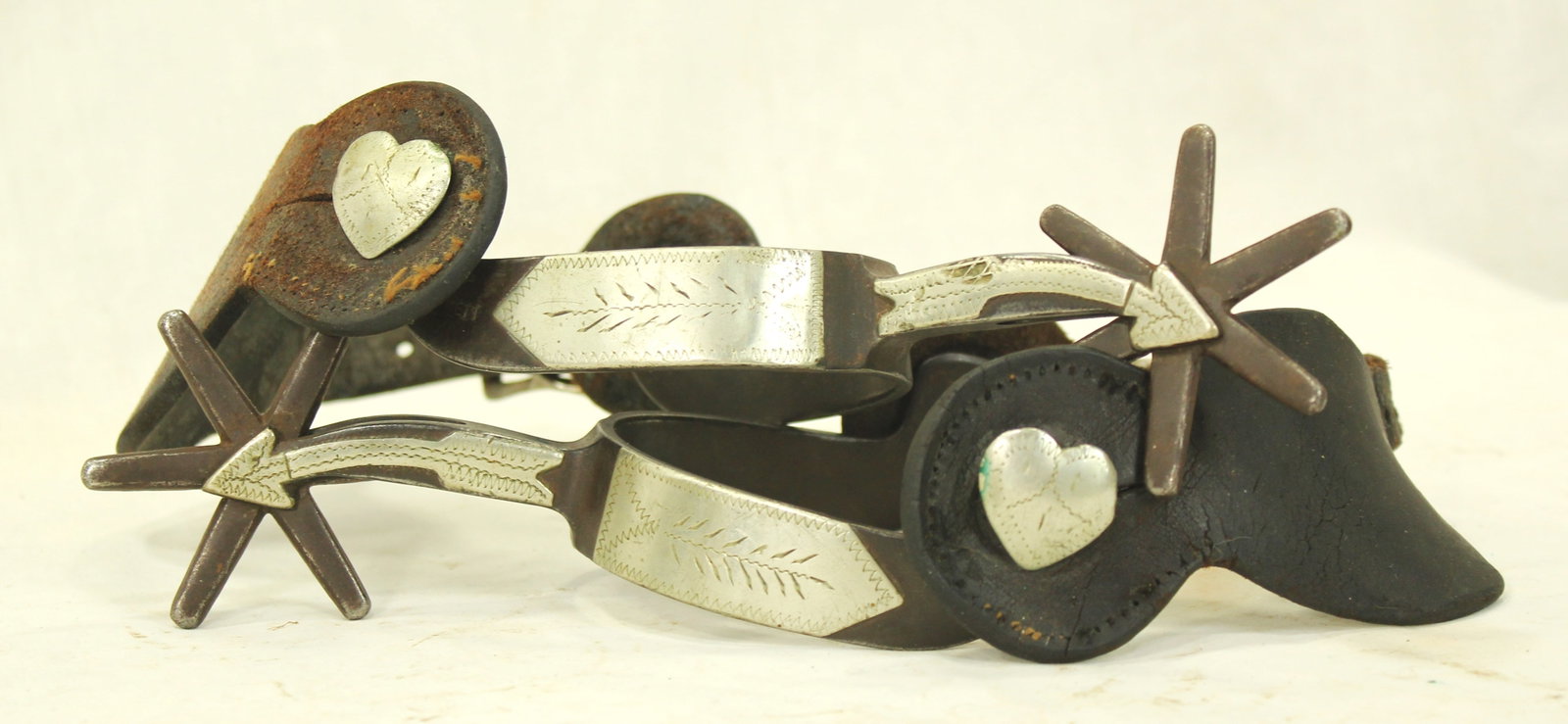Crockett Silver Spurs: Large pair of Crockett single mounted spurs featuring silver overlays and heart-shaped rowel strap buttons. Marked under the button, and completed by original straps.