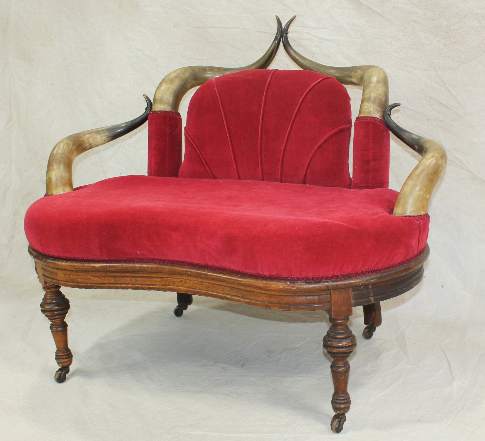 Antique Western Longhorn Settee Sofa: Exceptional longhorn horn loveseat featuring a carved hardwood base and red upholstered seat and back. Incorporating numerous matched horn elements forming the arms and crest rail. An impressive and