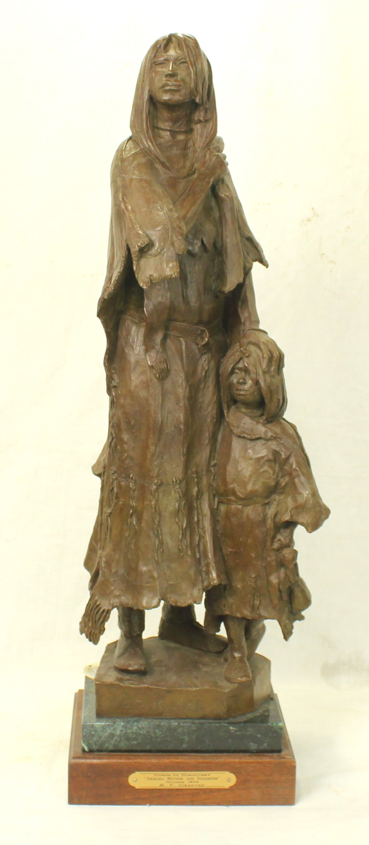 R.V. Greeves Bronze: A bronze 2004 sculpture titled “Arikara Mother and Daughter”. Mounted on wood base with title plaque. Numbered 1/30, and measuring 27”x 7”x 7”.