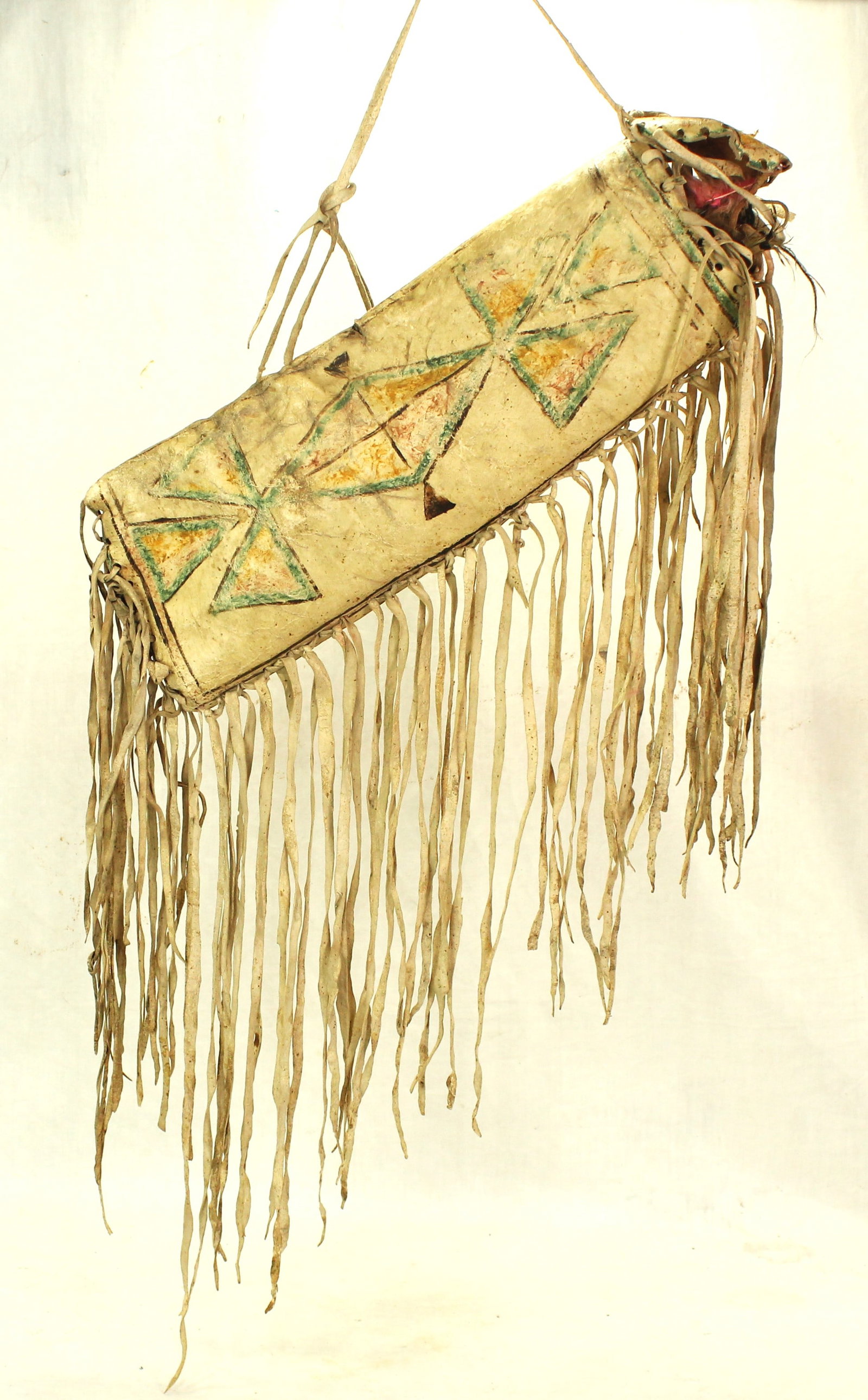 Northern Plains Parfleche Cylinder: Incredible 19th Century rawhide parfleche cylinder decorated with geometric painted motifs, and highlighted by extensive long fringe. With fantastic patina and style. With child’s game of