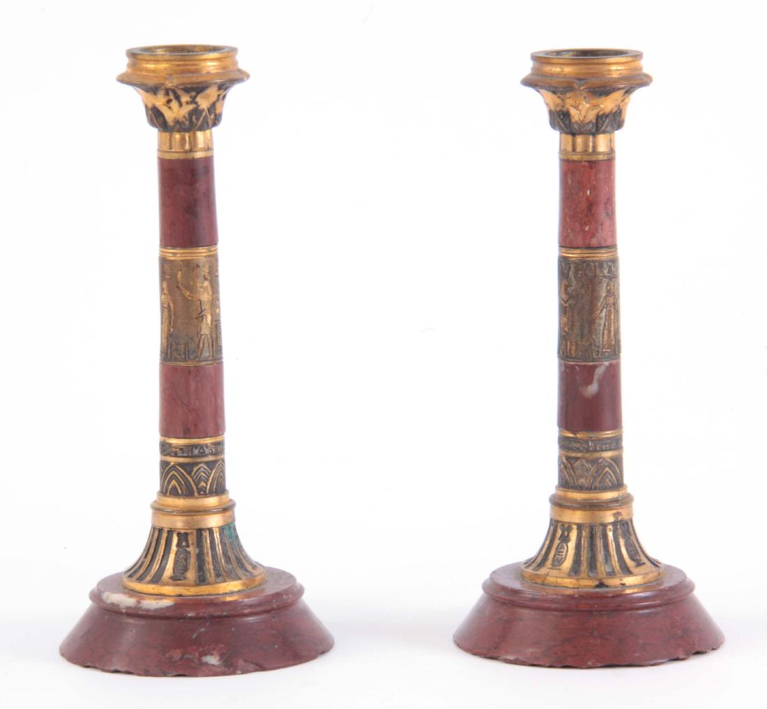 A pair of early 20th century Egyptianesque rouge m: A pair of early 20th century Egyptianesque rouge marble and ormolu candle sticks decorated with bands of hieroglyphics 18.5cm high x 8cm wide