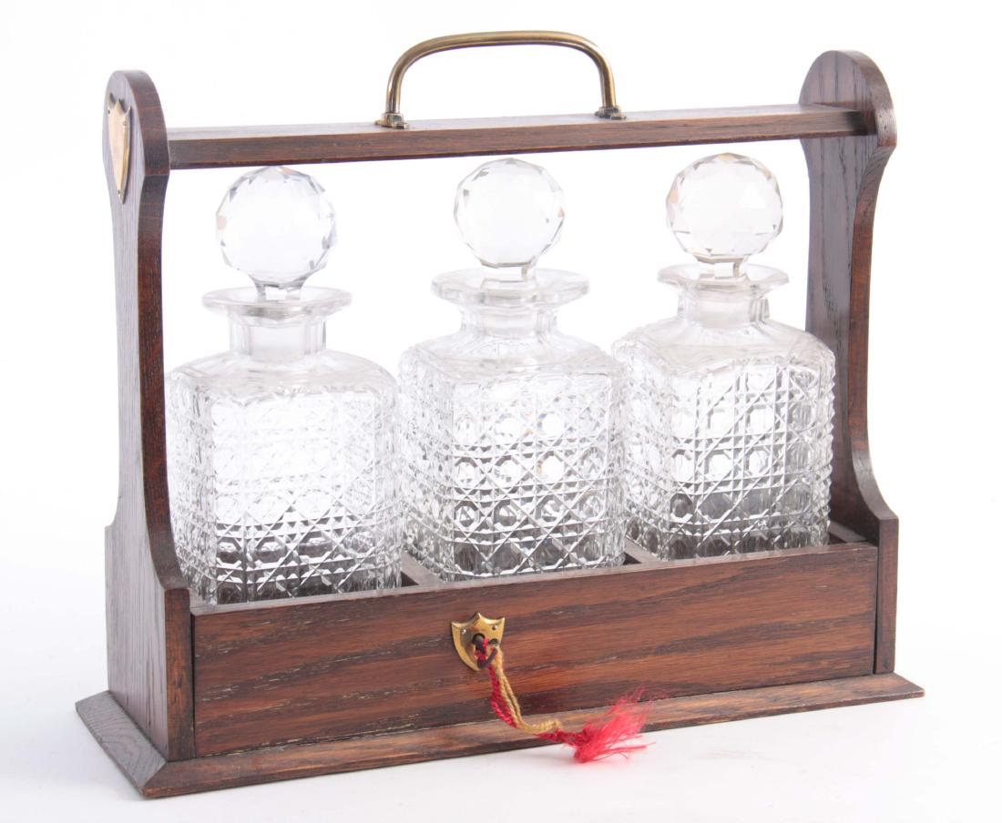 AN OAK THREE BOTTLE TANTALUS with cut glass bottle: AN OAK THREE BOTTLE TANTALUS with cut glass bottles 36cm wide 13cm deep 30cm high.