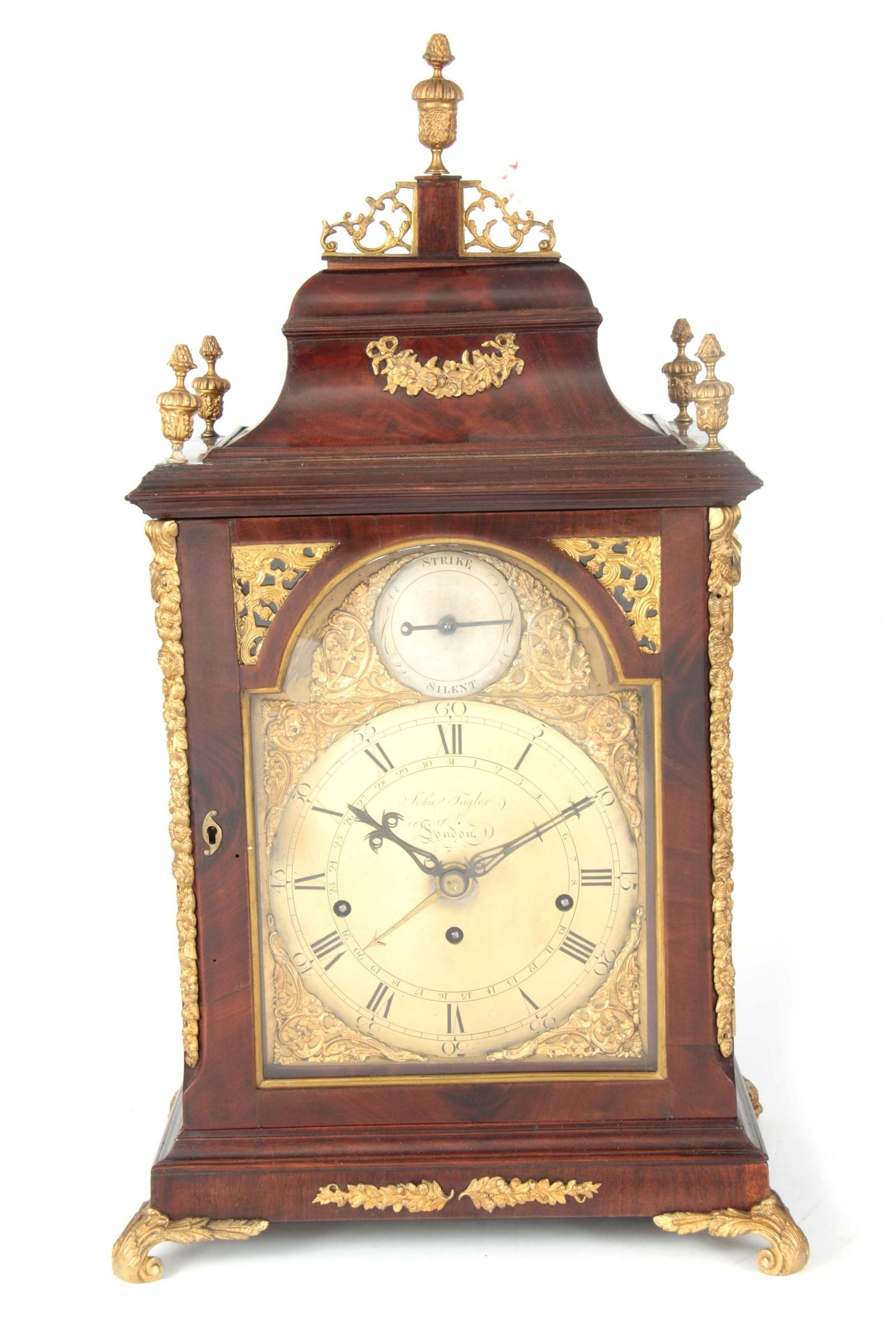 JOHN TAYLOR, LONDON A GEORGE III FIGURED MAHOGANY: JOHN TAYLOR, LONDON A GEORGE III FIGURED MAHOGANY ORMOLU MOUNTED QUARTER CHIMING BRACKET CLOCK the bell top pediment with urn finials above a glazed door with canted corners and applied floral relief