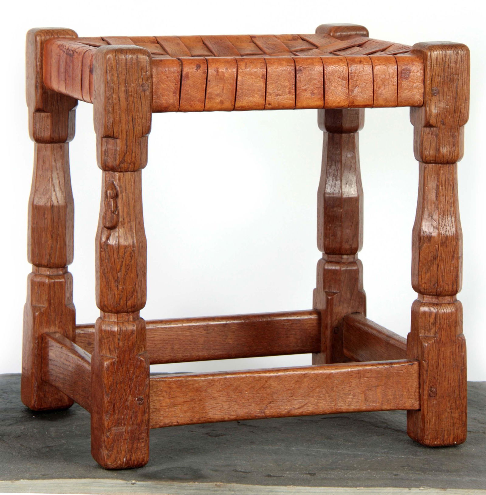A ROBERT 'MOUSEMAN' THOMPSON JOINT STOOL with inte: A ROBERT 'MOUSEMAN' THOMPSON JOINT STOOL with interlaced strapwork hide top above adzed faceted legs joined by side stretchers, one leg with carved mouse trademark 34cm wide 27cm deep 36cm high.