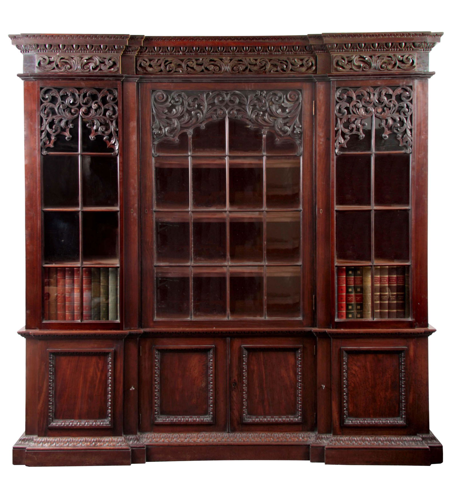 AN IMPRESSIVE 19TH CENTURY LOW WAISTED MAHOGANY IN: AN IMPRESSIVE 19TH CENTURY LOW WAISTED MAHOGANY INVERTED BREAKFRONT BOOKCASE IN THE MANNER OF WILLIAM KENT having egg and dart moulded cornice profusely carved with foliage above three glazed hinged d