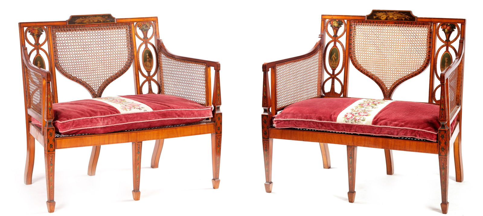 A PAIR OF 19TH CENTURY PAINTED SATINWOOD SHERATON STYLE: A PAIR OF 19TH CENTURY PAINTED SATINWOOD SHERATON STYLE TWO SEATER SETTEES with classical and floral painted decoration having Bergere shaped backs, sidearms, and seats with loose cushions; standing o