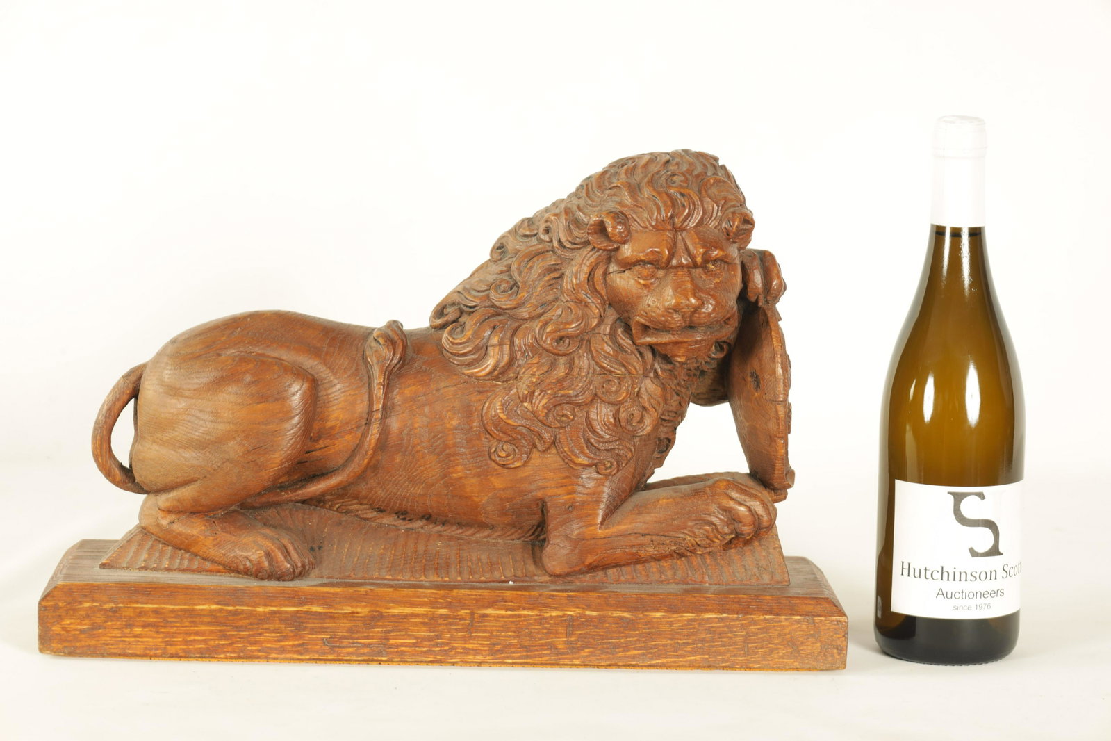 AN 18TH CENTURY CARVED OAK LION: AN 18TH CENTURY CARVED OAK LION in a recumbent pose holding a shield, mounted on a later plinth (27.5cm high 44cm wide)