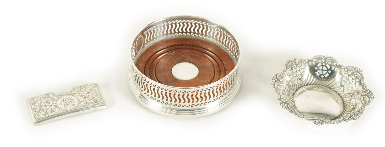 AN ELIZABETH II SILVER WINE BOTTLE COASTER WITH SOLID WOOD BASE, A LATE VICTORIAN SILVER CARD CASE: AN ELIZABETH II SILVER WINE BOTTLE COASTER WITH SOLID WOOD BASE and A LATE VICTORIAN SILVER CARD CASE of bowed open-top design with scrolled flower and leaf bright cut decoration. Chester 1900 and AN