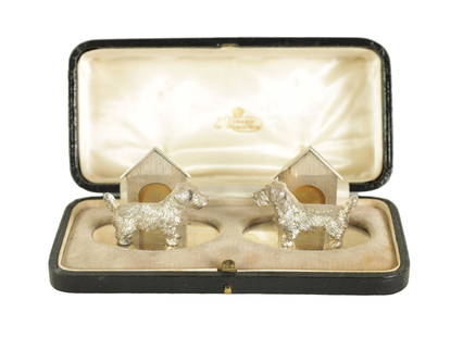 A CASED PAIR OF CAST SILVER NORFOLK TERRIER MENU HOLDERS: A CASED PAIR OF CAST SILVER NORFOLK TERRIER MENU HOLDERS on oval bases with dog house support, total approx weight 118g - by John Henry Hill, London, 1927-28. (5cm across)