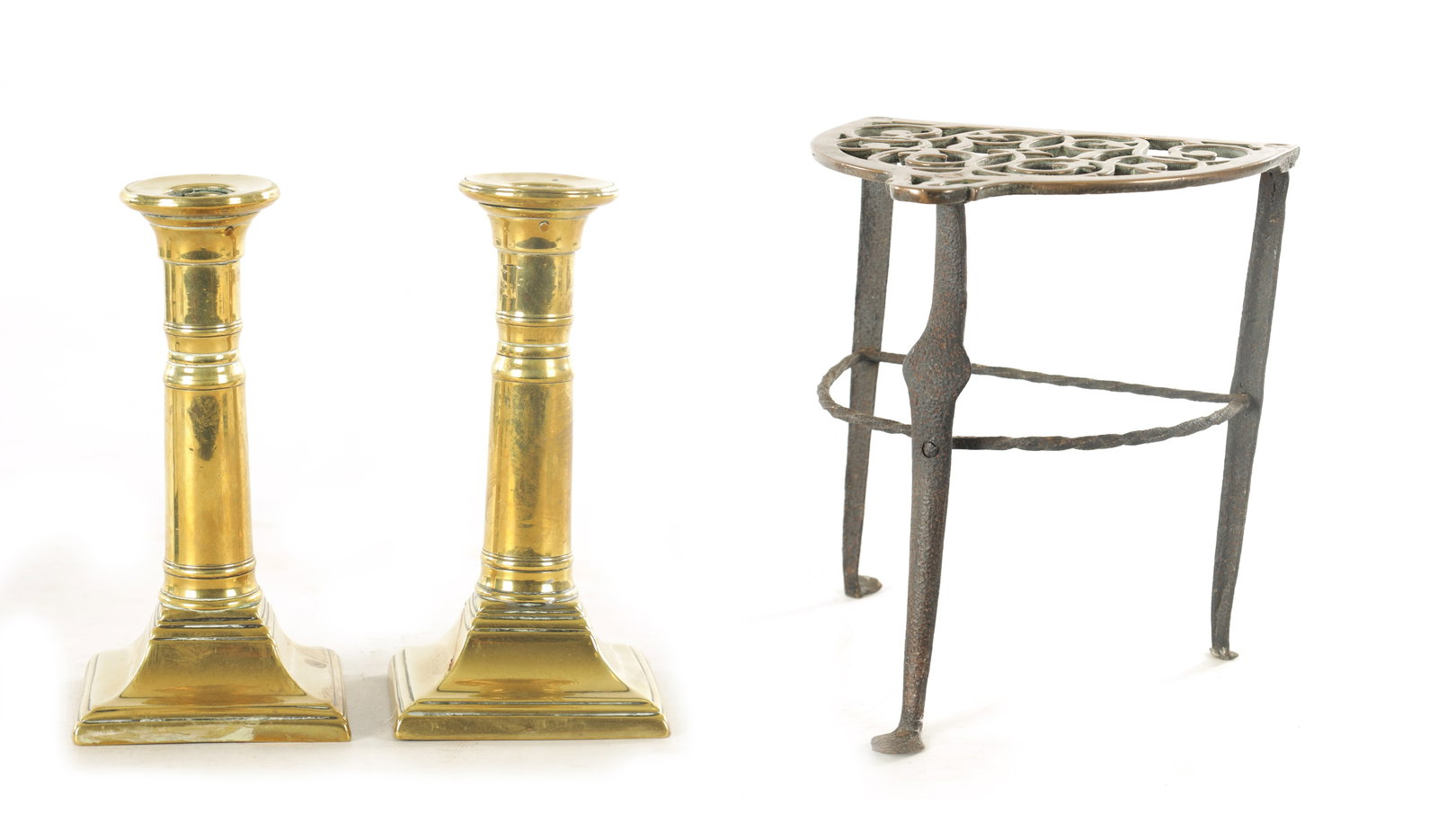 A PAIR OF GEORGE III BRASS CANDLESTICKS: A PAIR OF GEORGE III BRASS CANDLESTICKS with cannon barrel telescopic stems and square bases together with AN 18TH CENTURY IRON FRAMED CAST BELL METAL HEARTH TRIVET with bowed and scrolled cut-out top
