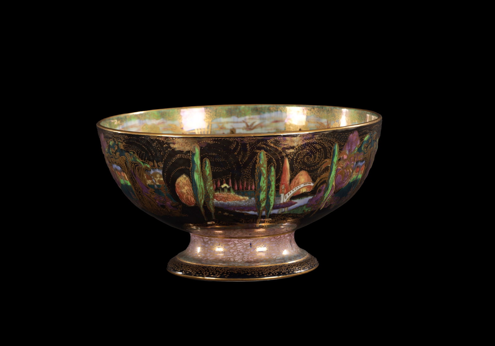A FINE WEDGWOOD FAIRYLAND LUSTRE PEDESTAL PUNCHBOWL CIRCA 1920'S DESIGNED BY DAISY MAKEIG-JONES: A FINE WEDGWOOD FAIRYLAND LUSTRE PEDESTAL PUNCHBOWL CIRCA 1920'S DESIGNED BY DAISY MAKEIG-JONES The gilded rim enclosing a continuous wooded river landscape scene with flying birds, figures and fairie