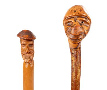 TWO LATE 19TH CENTURY FOLK ART CARVED HEAD WALKING STICKS: TWO LATE 19TH CENTURY FOLK ART CARVED HEAD WALKING STICKS depicting a man's head with a stained hat and a 'grotesque' man's head with a protruding nose and inset glass eyes; on painted shafts. (95.5cm