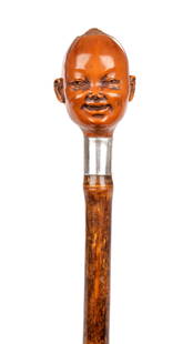 AN EARLY 20TH CENTURY CARVED COQUILLA NUT HANDLED WALKING STICK: AN EARLY 20TH CENTURY CARVED COQUILLA NUT HANDLED WALKING STICK modelled as a baby's head with dimpled cheeks above an inscribed silver collar, London, 1910, retailed by JKB; on a stained bamboo shaft