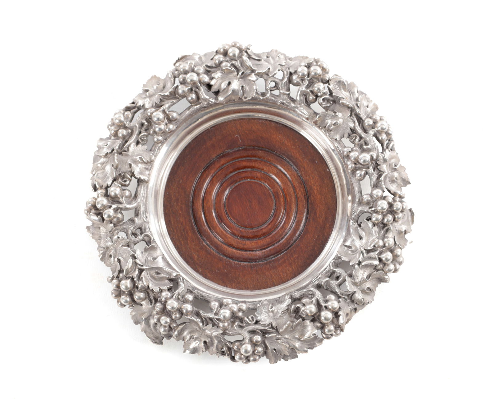 MORTIMER & HUNT, LONDON. A VICTORIAN MAHOGANY AND SILVER BOTTLE COASTER: MORTIMER & HUNT, LONDON. A VICTORIAN MAHOGANY AND SILVER BOTTLE COASTER the frame cast and pierced as trailing grape vine, raised on three scroll feet, with turned wooden base, 1841, App. 802g (21cm d