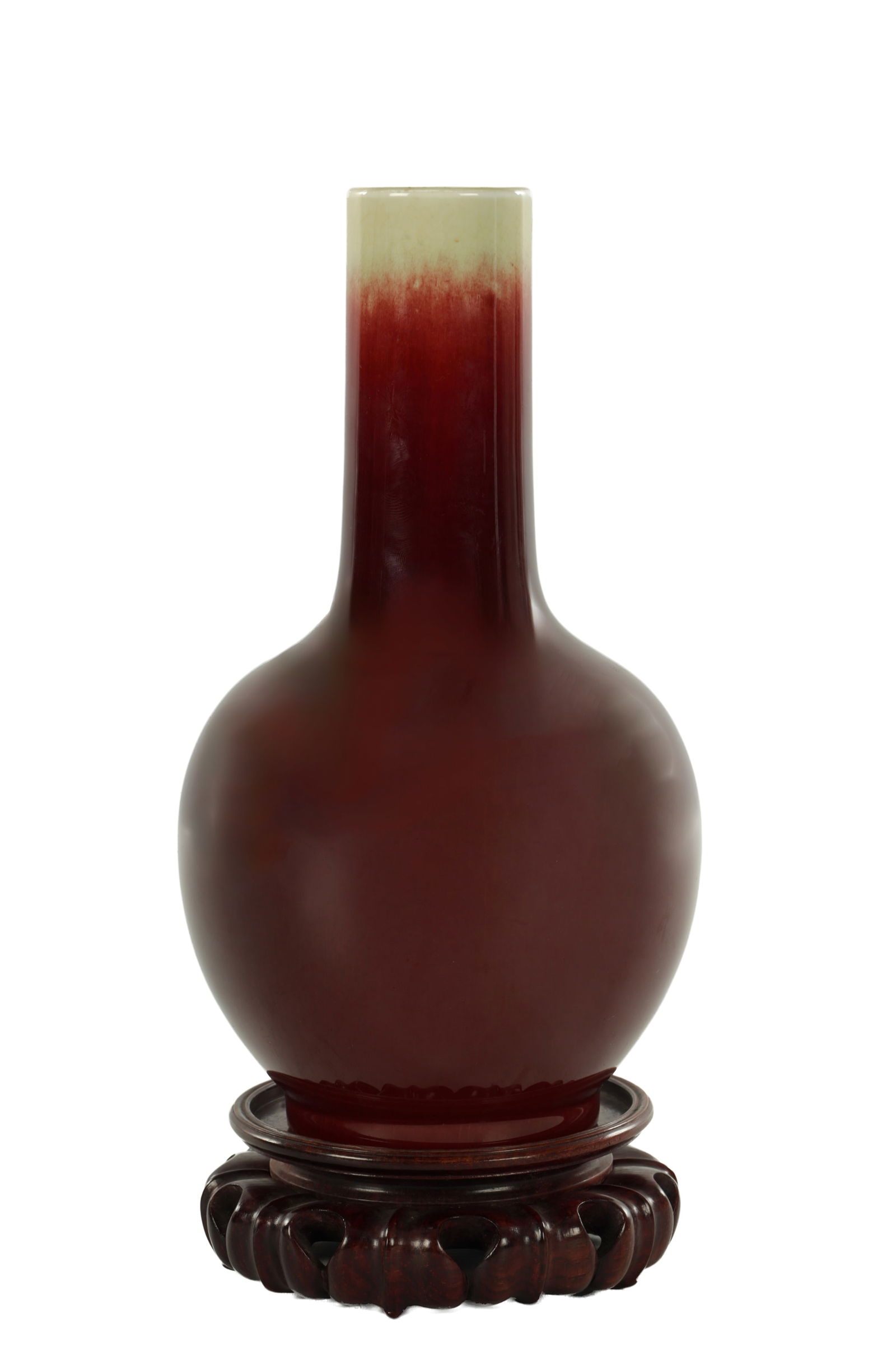 A CHINESE SAND DE BOEUF OXBLOOD PORCELAIN VASE ON STAND: A CHINESE SAND DE BOEUF OXBLOOD PORCELAIN VASE ON STAND of bulbous form with cylindrical neck and celadon glazed rim, standing on a carved wooden base. (27cm high including stand)