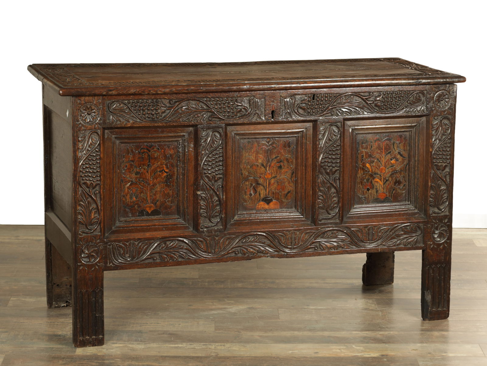 A 17TH CENTURY YORKSHIRE CARVED OAK AND MARQUETRY PANELLED COFFER: A 17TH CENTURY YORKSHIRE CARVED OAK AND MARQUETRY PANELLED COFFER with plank top having grape and leaf carved border enclosing three floral marquetry panels raised on tall stile feet (138cm wide 57cm