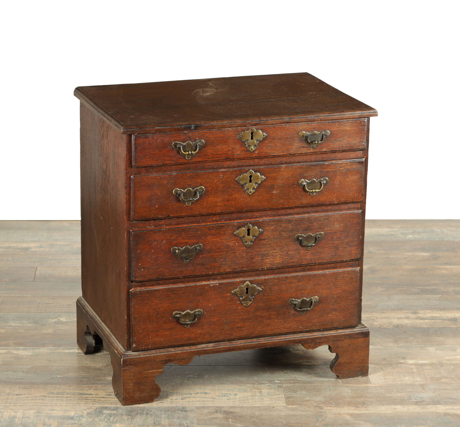 A GEORGE II OAK CHEST OF DRAWERS OF SMALL SIZE: A GEORGE II OAK CHEST OF DRAWERS OF SMALL SIZE with moulded edge too above four graduated drawers fitted with solid brass handles and raised on shaped bracket feet (64cm wide 44cm deep 69cm high )