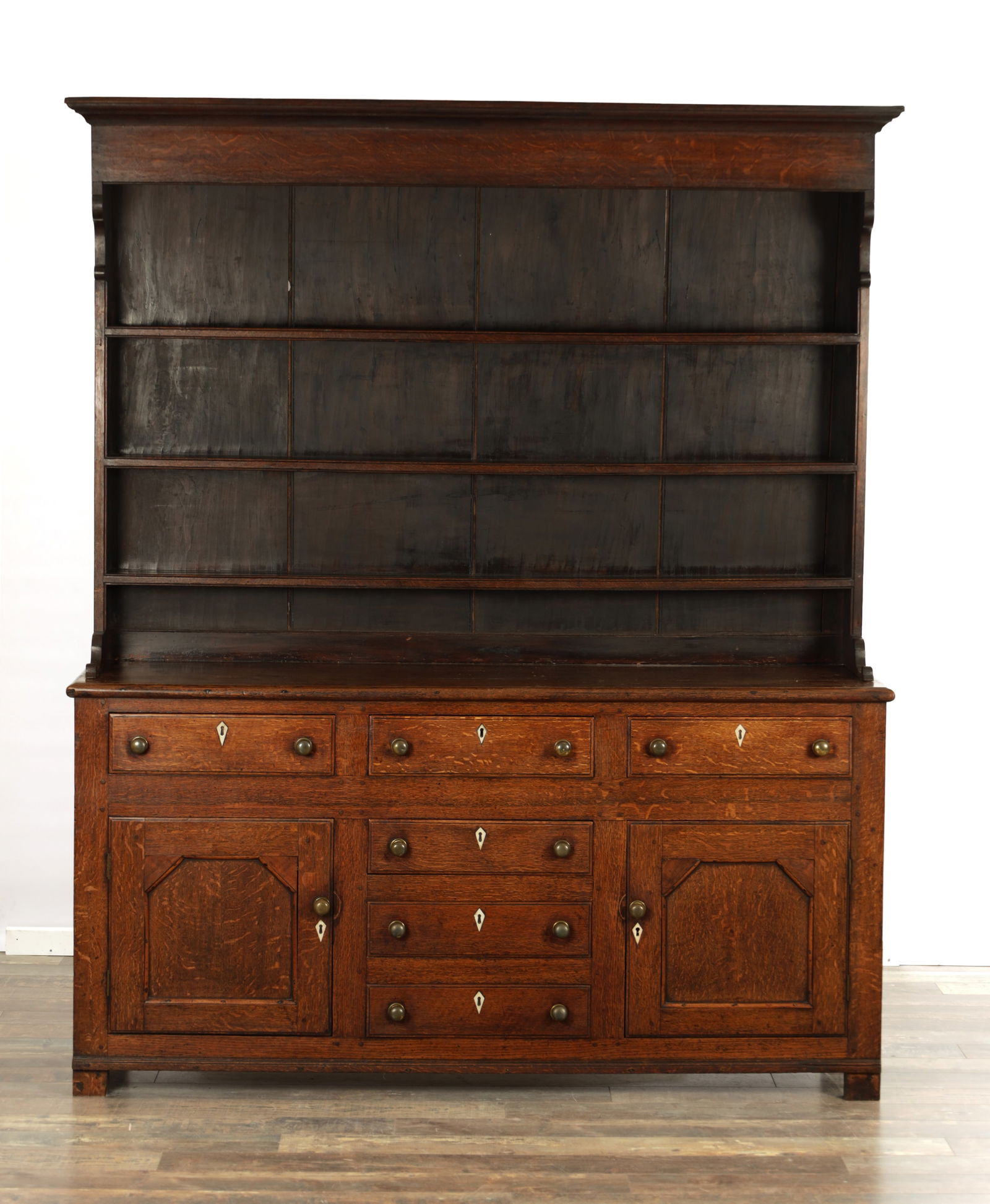 A LATE GEORGIAN OAK CUPBOARD DRESSER AND RACK: A LATE GEORGIAN OAK CUPBOARD DRESSER AND RACK with moulded cornice above three shelves with painted back boards, above a cupboard base with a bank of central drawers and cupboard doors to each side, f