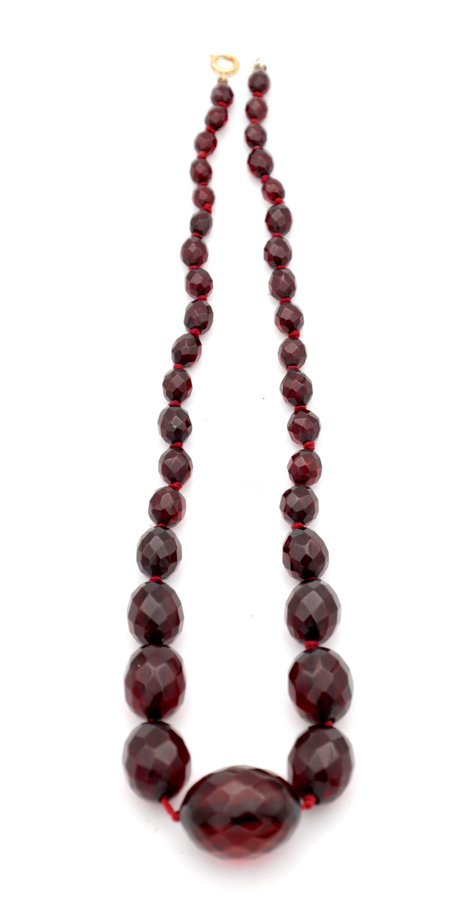 A GRADUATED CHERRY AMBER BAKELITE FACETED BEAD NECKLACE: A GRADUATED CHERRY AMBER BAKELITE FACETED BEAD NECKLACE on a red string with a spring ring clasp, the largest bead measuring 25mm, total app. weight 36.3g. (Length of the necklace 49cm)