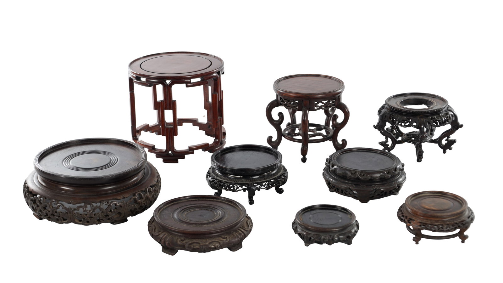 A COLLECTION OF NINE CHINESE CARVED HARDWOOD STANDS: A COLLECTION OF NINE CHINESE CARVED HARDWOOD STANDS of varying circular forms with recessed tops and carved or pierced aprons, raised on scroll or cabriole supports. (Tallest 21cm, widest 29cm)