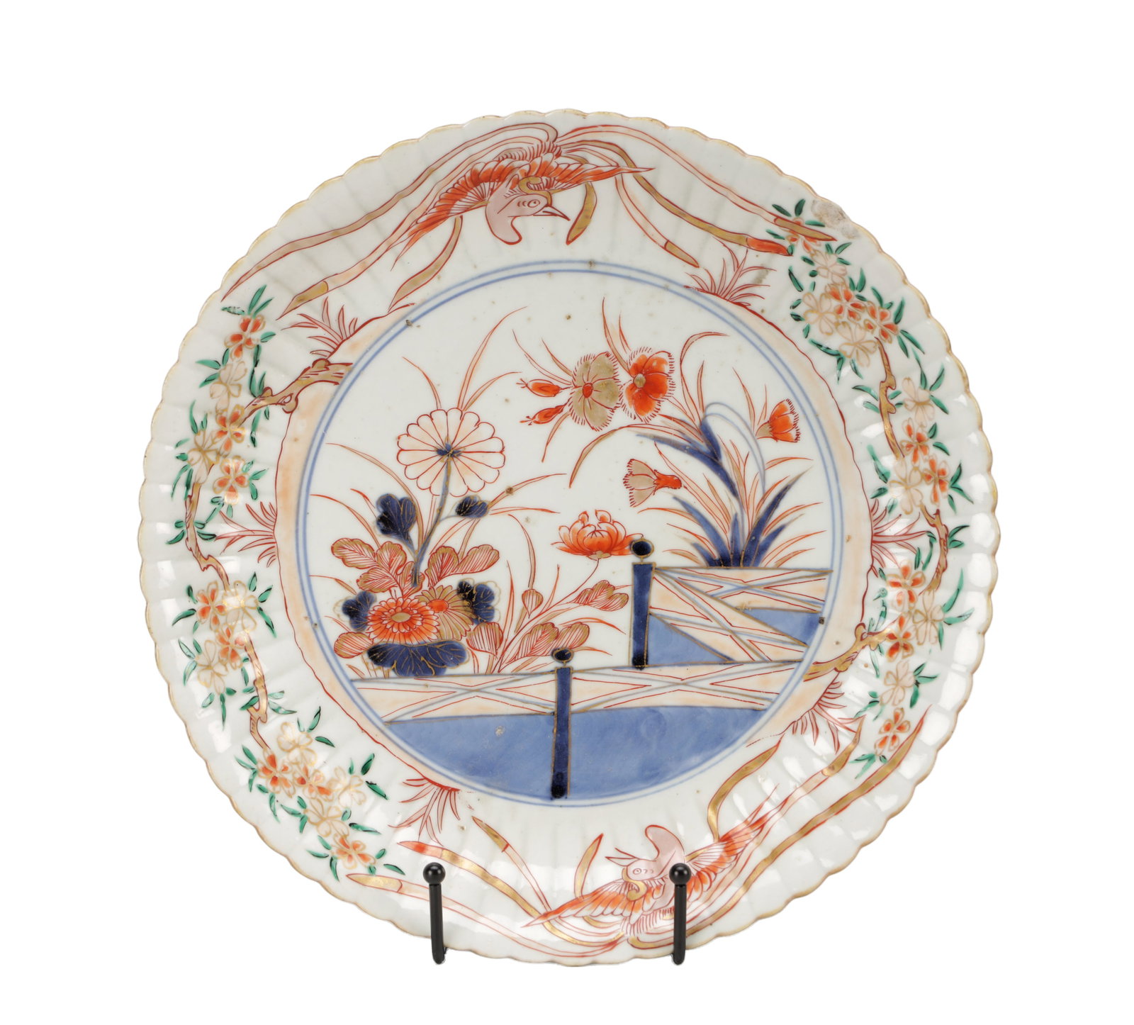 A 19TH CENTURY JAPANESE IMARI PORCELAIN PLATE: A 19TH CENTURY JAPANESE IMARI PORCELAIN PLATE of circular form with a scalloped rim, enamelled in underglaze blue and iron-red with green highlights depicting a fenced garden with floral sprays within