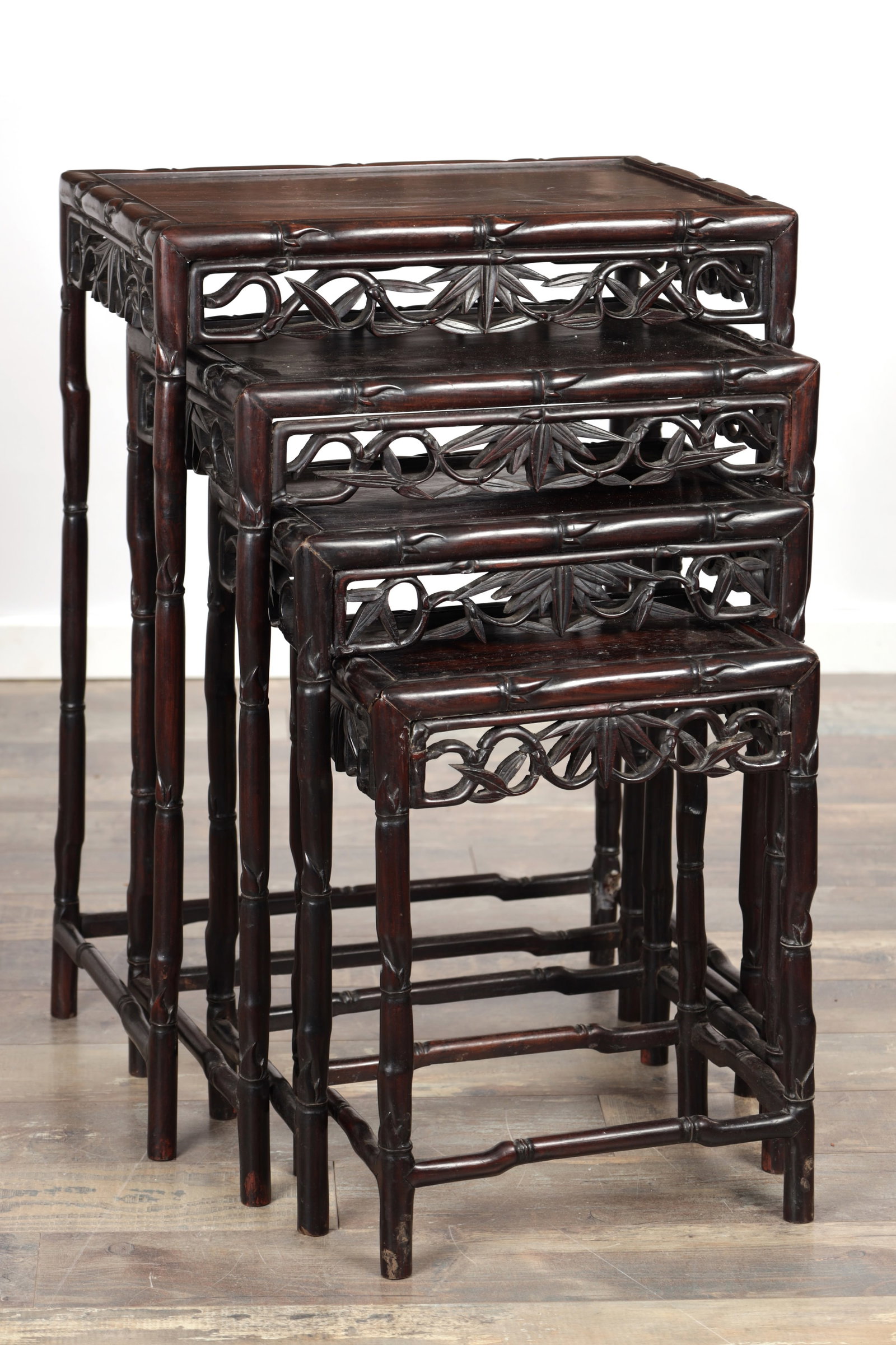 A SET OF FOUR 19TH CENTURY CHINESE CARVED HARDWOOD NEST OF TABLES: A SET OF FOUR 19TH CENTURY CHINESE CARVED HARDWOOD NEST OF TABLES each rectangular with plain tops and pierced foliate friezes, the frames carved in bamboo form, raised on straight legs united by stre