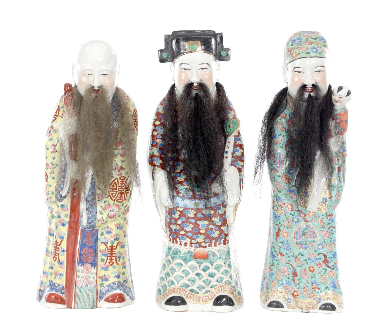 THREE CHINESE FAMILLE ROSE PORCELAIN FIGURES OF IMMORTALS: THREE CHINESE FAMILLE ROSE PORCELAIN FIGURES OF IMMORTALS each modelled standing in flowing robes painted with floral and symbolic decoration, two wearing official headdresses and one holding a child,