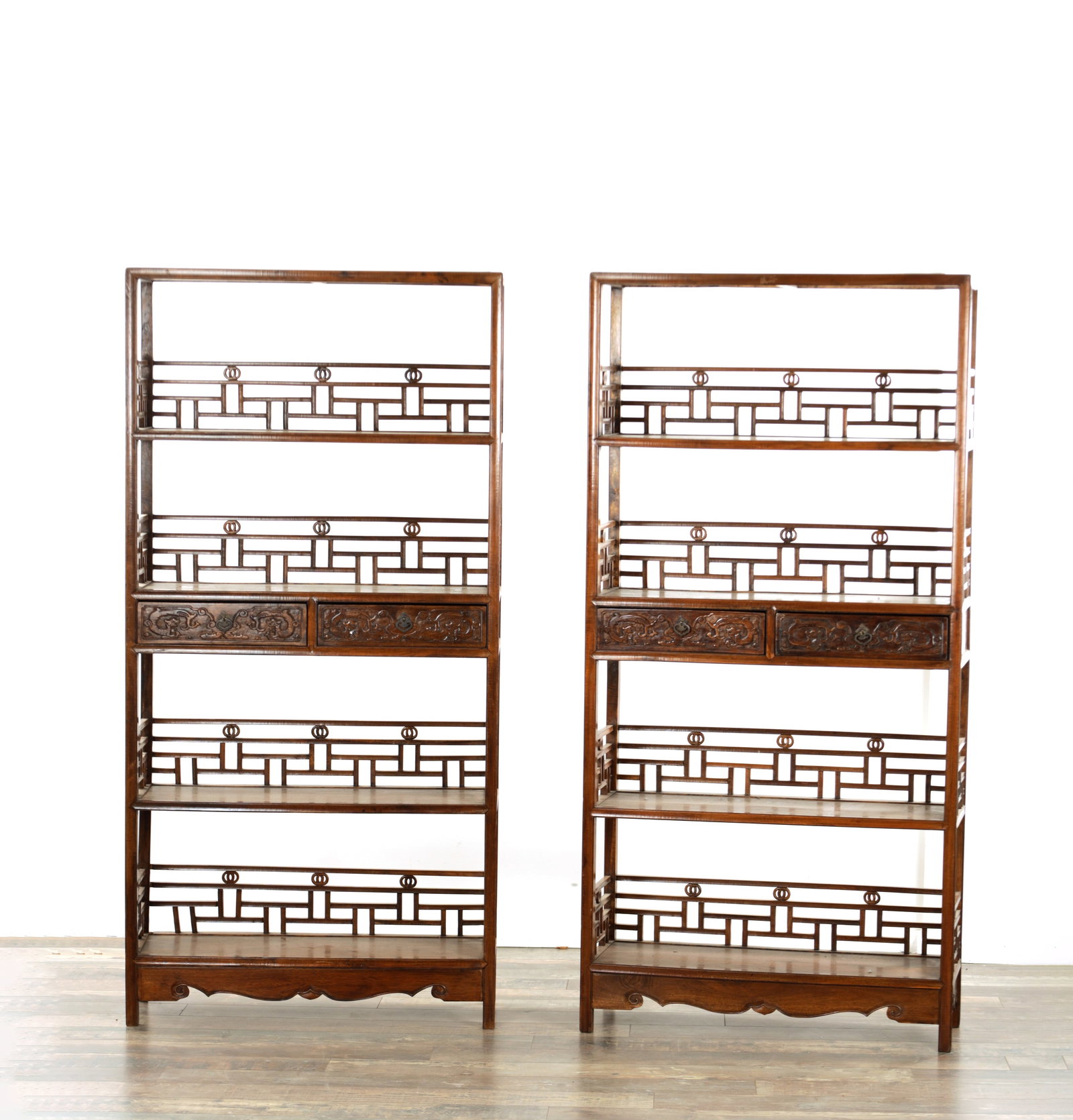 A PAIR OF CHINESE HARDWOOD DISPLAY CABINETS: A PAIR OF CHINESE HARDWOOD DISPLAY CABINETS comprising of open shelves with fretted backs and craved frieze drawers to the centre (86cm wide 31cm deep 176cm high)
