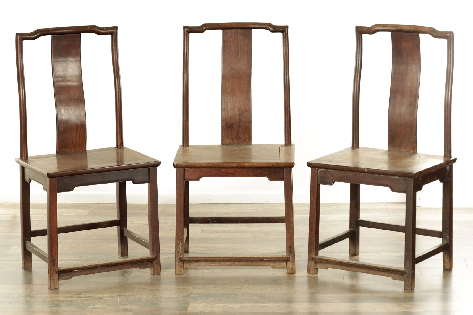 A SET OF THREE 19TH CENTURY CHINESE HARDWOOD SIDE CHAIRS: A SET OF THREE 19TH CENTURY CHINESE HARDWOOD SIDE CHAIRS with solid back splats and shaped top rails above panelled seats raised on square legs joined by under stretchers. (54cm wide 108cm high )