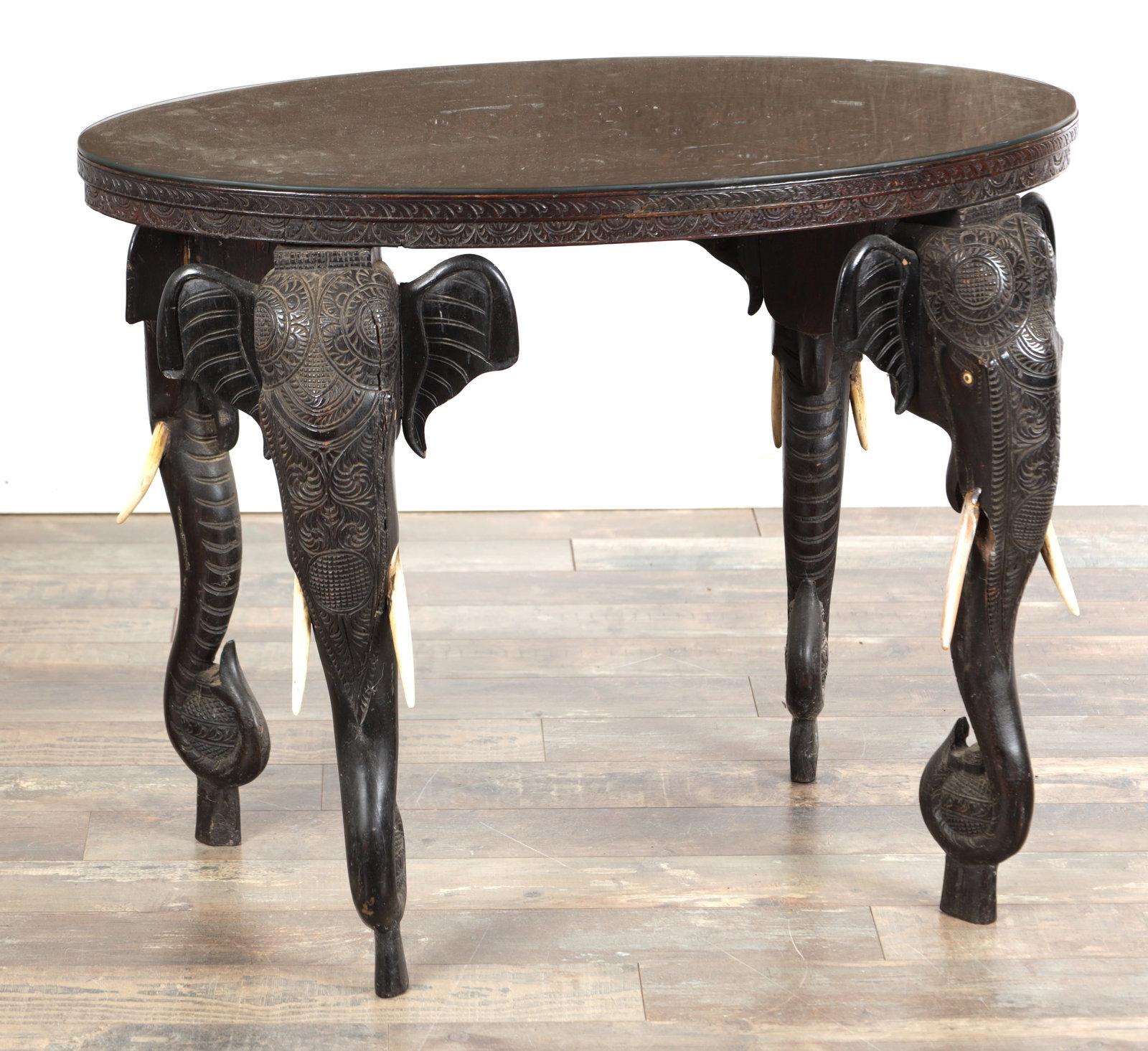 A 19TH CENTURY ANGLO-INDIAN CARVED ROSEWOOD OCCASIONAL TABLE WITH ELEPHANT MASK LEGS: A 19TH CENTURY ANGLO-INDIAN CARVED ROSEWOOD OCCASIONAL TABLE WITH ELEPHANT MASK LEGS of oval form with a foliate-carved moulded edge and carved frieze, raised on four elephant head supports with scrol