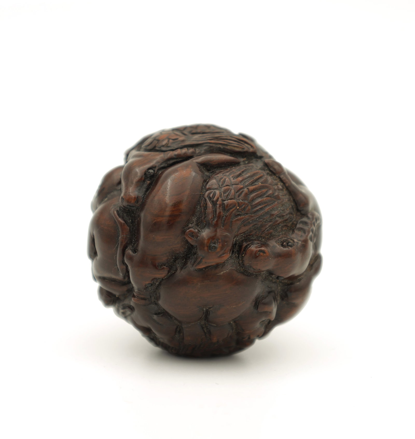 A JAPANESE MEIJI PERIOD CARVED HARDWOOD NETSUKE: A JAPANESE MEIJI PERIOD CARVED HARDWOOD NETSUKE of spherical form modelled as various animals with black beaded eyes, signed. (45mm diameter)