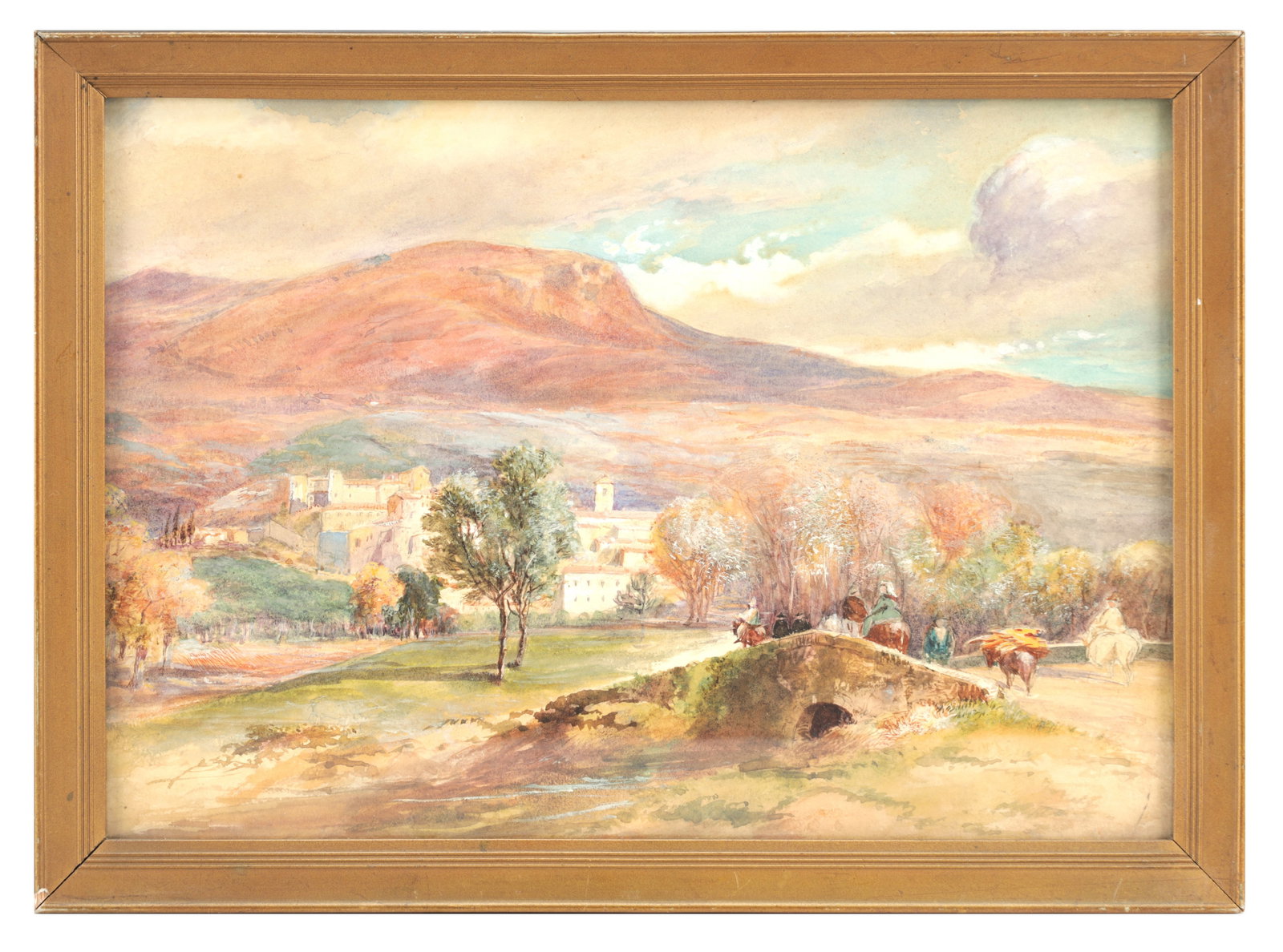 AN ITALIAN WATERCOLOUR LANDSCAPE: AN ITALIAN WATERCOLOUR LANDSCAPE depicting a mountainous view with a hill town, trees and figures with pack animals crossing a small stone bridge, mounted in a gilt frame. (24cm high, 34.5cm wide)