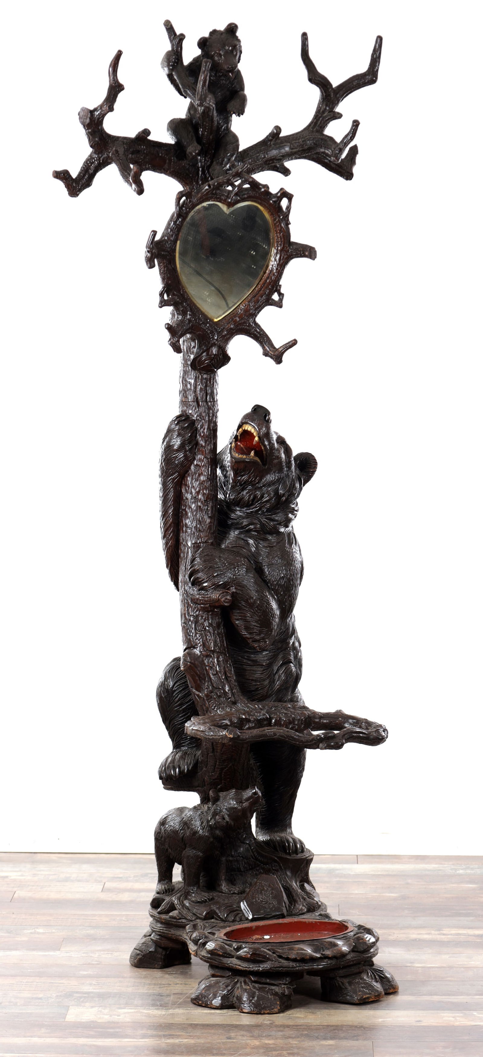 A 19TH CENTURY BLACK FOREST CARVED LINDEN WOOD BEAR HALL STAND WITH HEART-SHAPED MIRROR: A 19TH CENTURY BLACK FOREST CARVED LINDEN WOOD BEAR HALL STAND WITH HEART-SHAPED MIRROR the branching crest with a seated cub and coat hooks above a heart-shaped mirror, the naturalistic trunk climbed