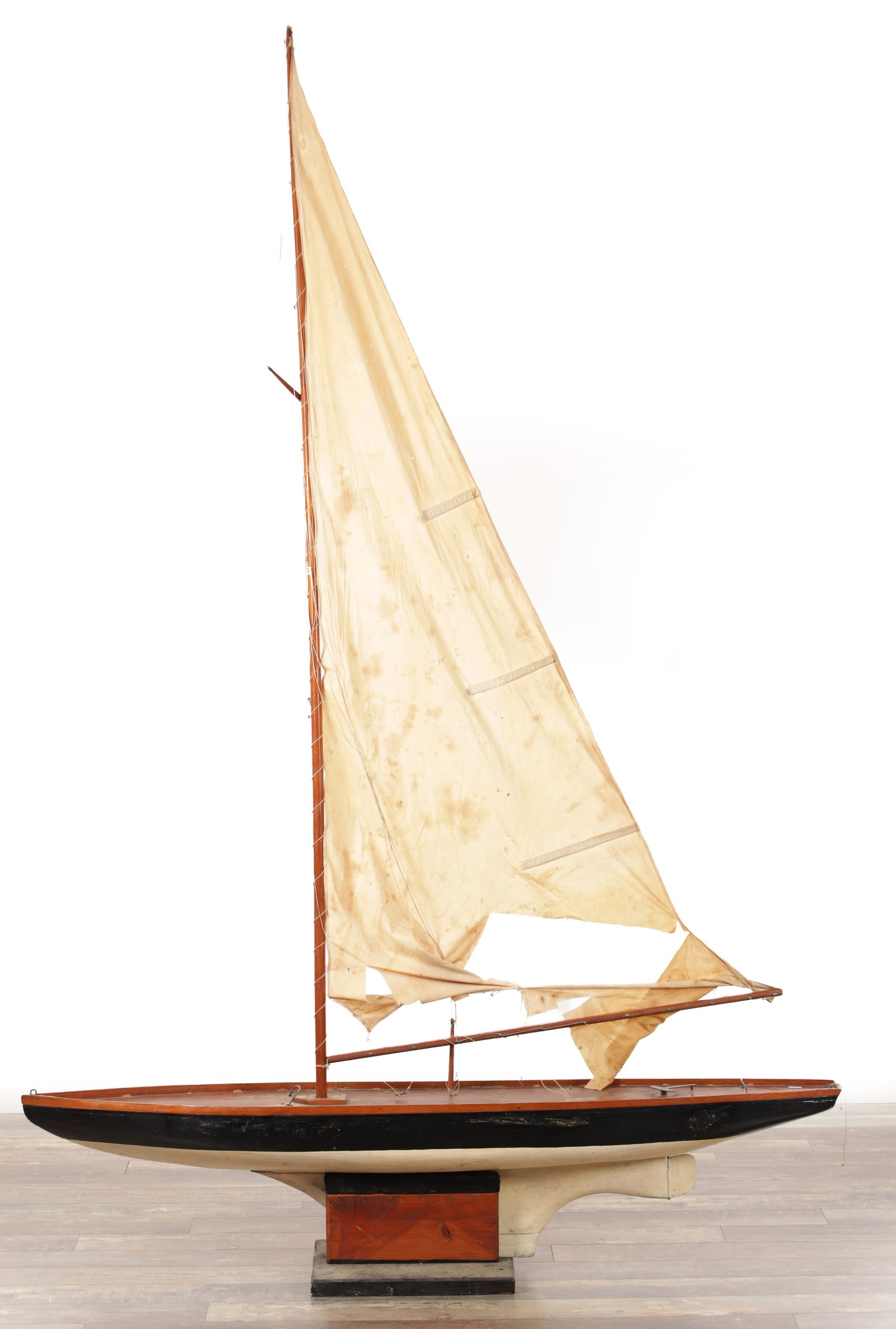 A LARGE 19TH CENTURY PAINTED WOOD POND YACHT WITH COTTON SAILS ON STAND: A LARGE 19TH CENTURY PAINTED WOOD POND YACHT WITH COTTON SAILS ON STAND with varnished deck and black topsides over a cream-painted hull, single wooden mast with mainsail and jib on a bowsprit, fitted