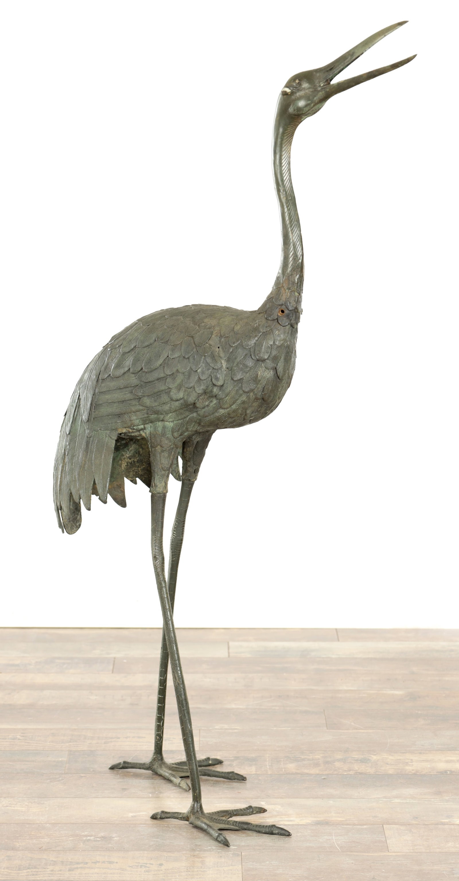 A GREEN PATINATED BRONZE GARDEN SCULPTURE OF A HERON: A GREEN PATINATED BRONZE GARDEN SCULPTURE OF A HERON naturalistically modelled standing with head raised and beak open, with detailed plumage, long slender legs and splayed toes. (122cm high )