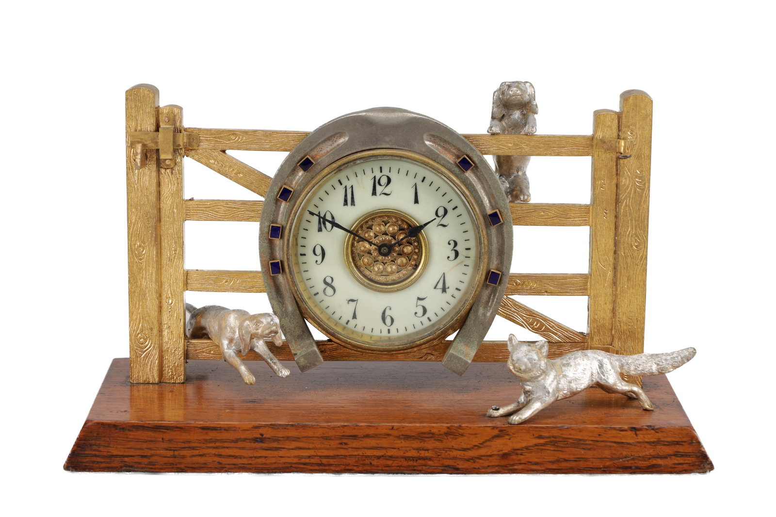 A LATE 19TH CENTURY GILT AND SILVERED BRASS FOX AND HOUNDS MANTEL CLOCK WITH HORSESHOE BEZEL ON OAK: A LATE 19TH CENTURY GILT AND SILVERED BRASS FOX AND HOUNDS MANTEL CLOCK WITH HORSESHOE BEZEL ON OAK BASE of farm gate form with a circular cream dial and Arabic numerals within a cast horseshoe mount