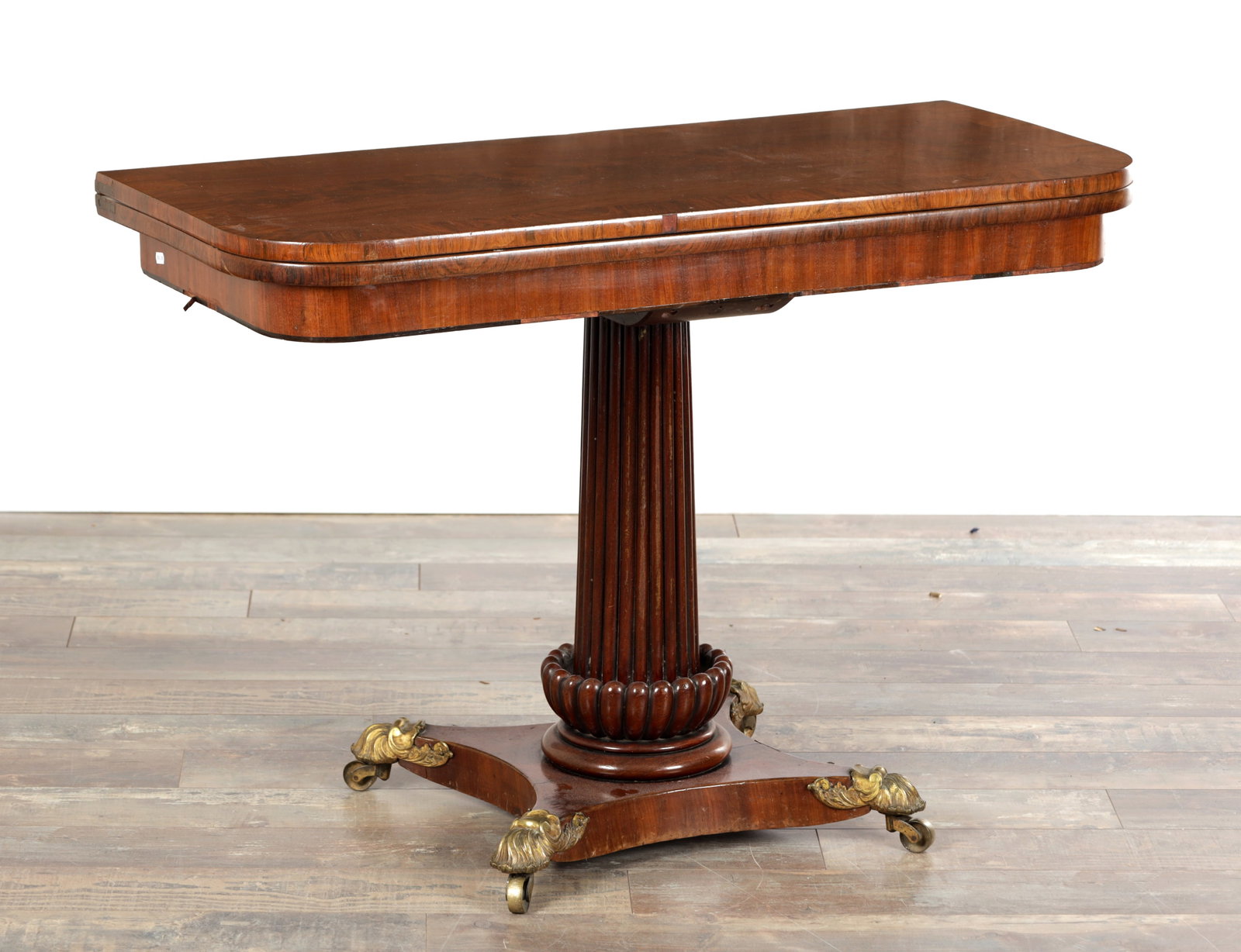 A REGENCY FIGURED MAHOGANY FOLD-OVER TEA TABLE ON A REEDED PEDESTAL BASE: A REGENCY FIGURED MAHOGANY FOLD-OVER TEA TABLE ON A REEDED PEDESTAL BASE of rounded rectangular form with a moulded edge, the hinged top over a reeded tapering column with lobed collar, raised on a co