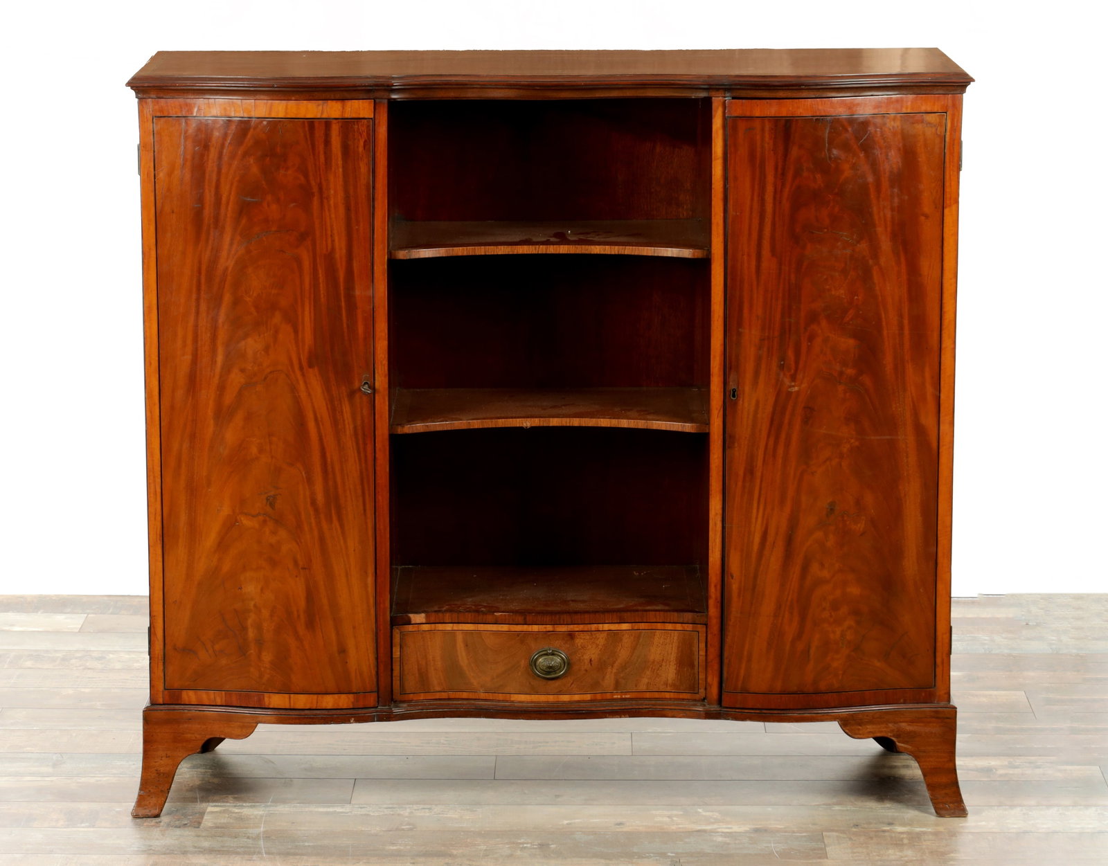 AN UNUSUAL GEORGE III CROSS-BANDED FLAMED MAHOGANY SERPENTINE FRONTED SIDE CABINET: AN UNUSUAL GEORGE III CROSS-BANDED FLAMED MAHOGANY SERPENTINE FRONTED SIDE CABINET with side cupboards revealing adjustable shelves flanking an open-shelved centre with bottom drawers; raised on splay