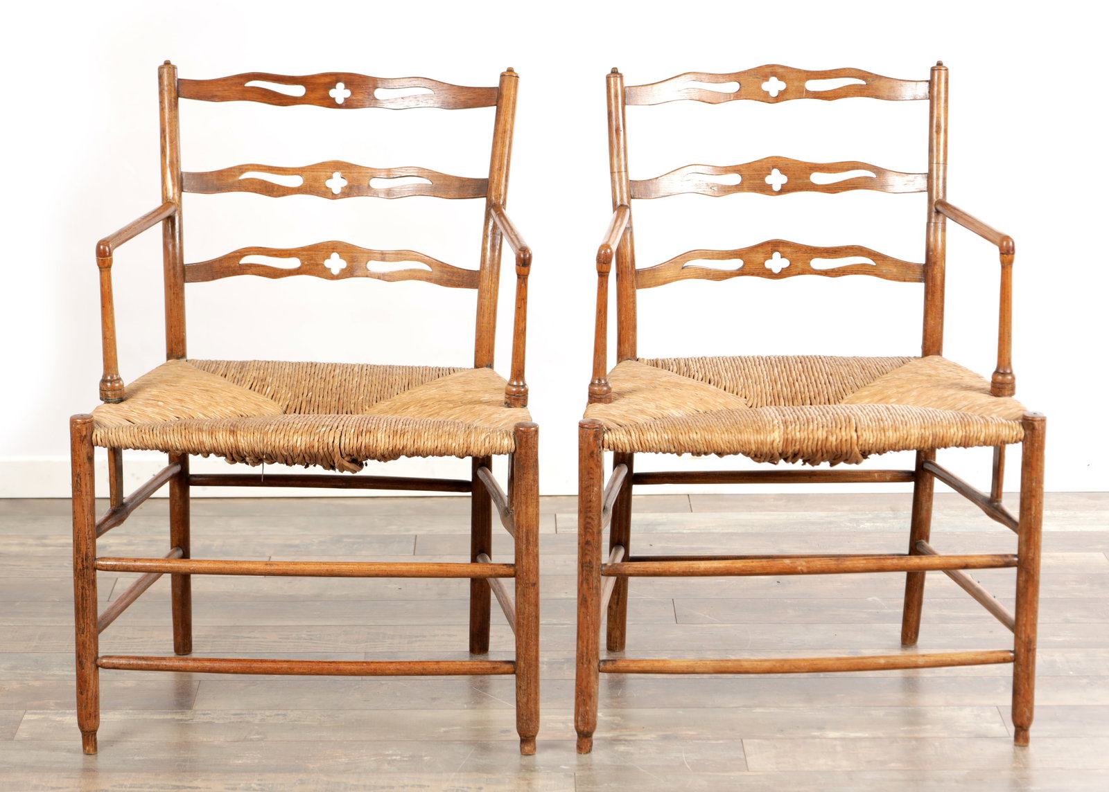A PAIR OF 19TH CENTURY ENGLISH LADDERBACK ARMCHAIRS WITH RUSH SEATS: A PAIR OF 19TH CENTURY ENGLISH LADDERBACK ARMCHAIRS WITH RUSH SEATS each with three shaped splats pierced with central quatrefoils, straight open arms on turned supports, woven rush seats, raised on s