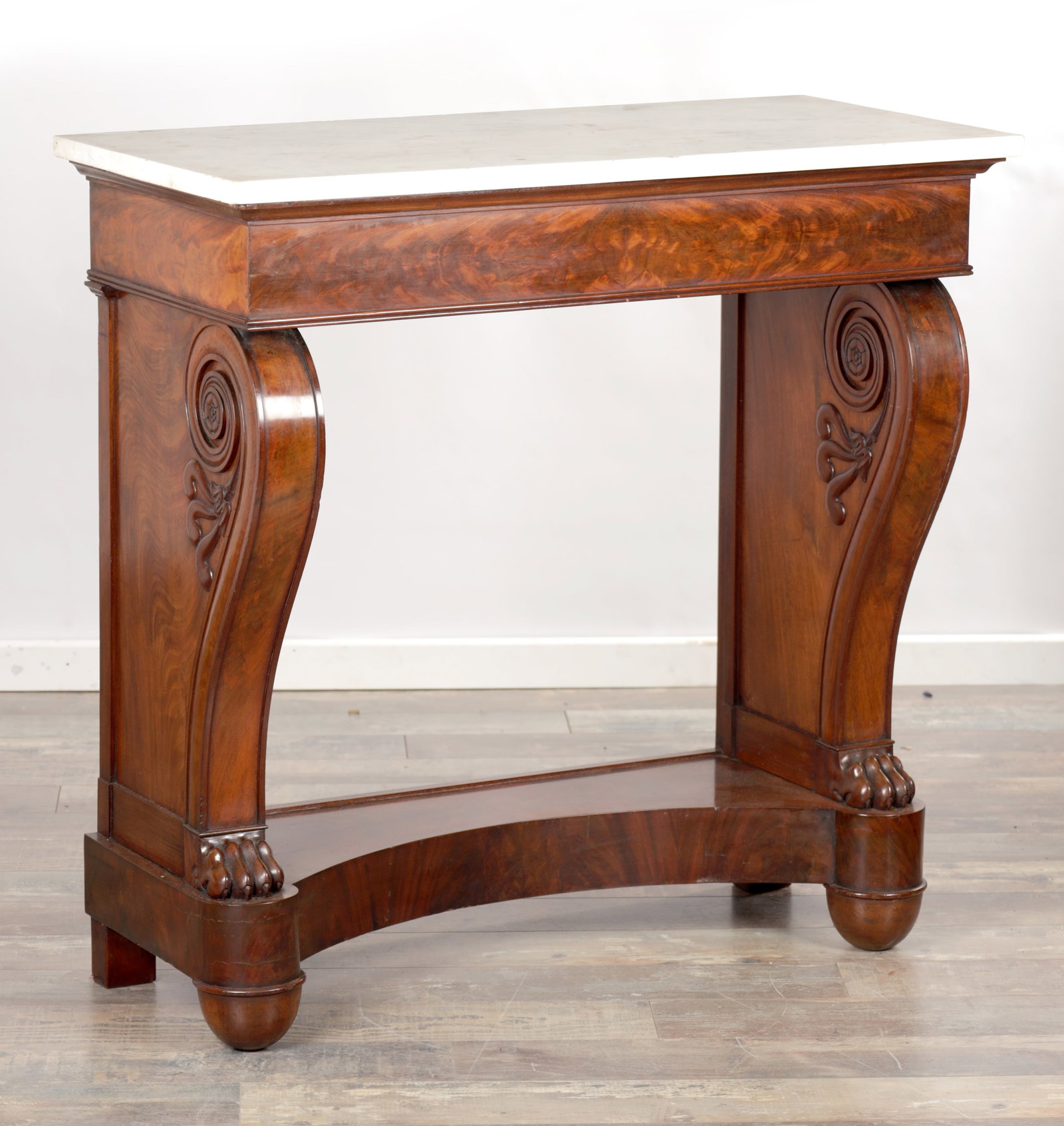 AN EARLY 19TH CENTURY MAHOGANY CONSOLE TABLE WITH WHITE MARBLE TOP: AN EARLY 19TH CENTURY MAHOGANY CONSOLE TABLE WITH WHITE MARBLE TOP the rectangular top above a plain frieze, the scroll supports carved with volutes and foliate detail, raised on a concave front platf