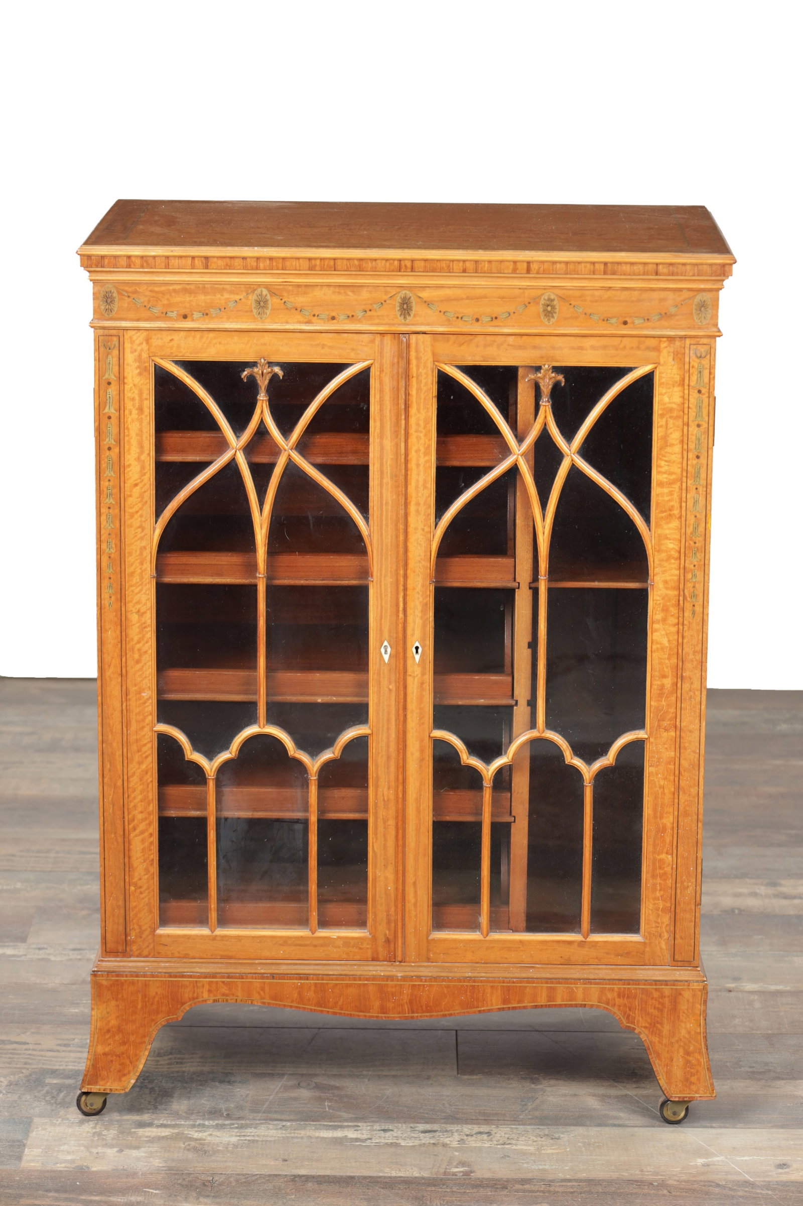 A LATE 19TH CENTURY PAINTED SATINWOOD AND INLAID GLAZED CABINET: A LATE 19TH CENTURY PAINTED SATINWOOD AND INLAID GLAZED CABINET with a moulded top above a frieze painted with Adam style swags and paterae, the twin gothic astragal glazed doors enclosing adjustable
