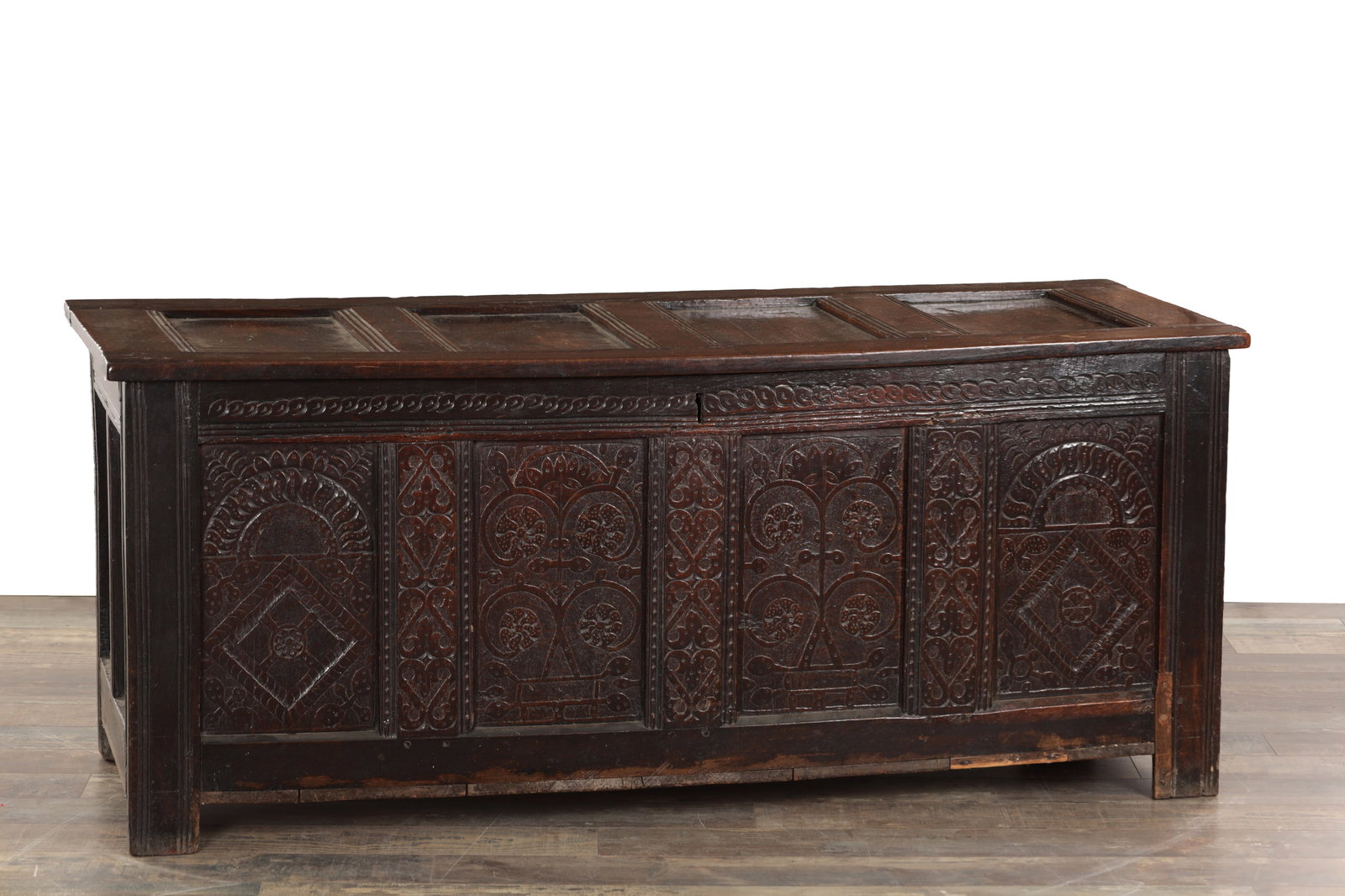 A 17TH CENTURY ENGLISH OAK PANELLED COFFER: A 17TH CENTURY ENGLISH OAK PANELLED COFFER with a hinged panelled lid above a four-panel front carved with lunettes, lozenges and stylised foliate roundels, the frieze guilloche carved, panelled sides