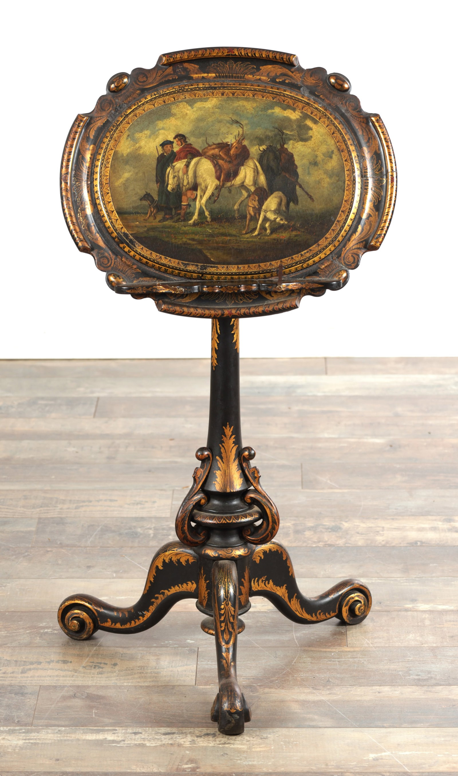 A 19TH CENTURY PAPIER MACHE LACQUERWORK ADJUSTABLE MUSIC TABLE WITH A PAINTED SCOTTISH HUNTING SCENE: A 19TH CENTURY PAPIER MACHE LACQUERWORK ADJUSTABLE MUSIC TABLE WITH A PAINTED SCOTTISH HUNTING SCENE the shaped cartouche top finely painted with huntsmen, hounds and stag within gilt foliate borders