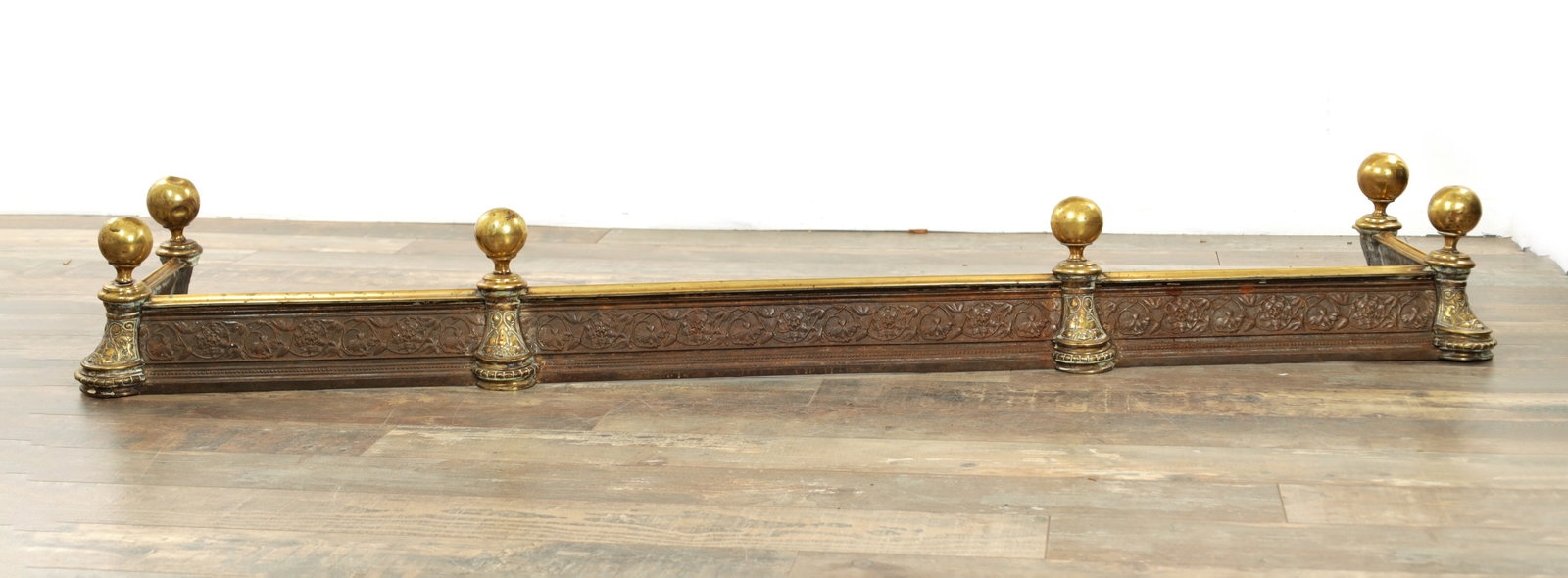 A LATE 19TH CENTURY CAST IRON AND BRASS AESTHETIC PERIOD HEARTH FENDER: A LATE 19TH CENTURY CAST IRON AND BRASS AESTHETIC PERIOD HEARTH FENDER with leaf work cast front and round finials. (172cm wide 40cm deep )