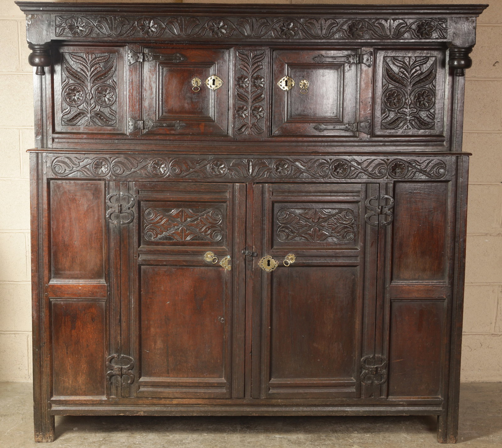 A LATE 17TH CENTURY ENGLISH JOINED OAK COURT CUPBOARD WITH CARVED FRIEZES AND PANELLED DOORS: A LATE 17TH CENTURY ENGLISH JOINED OAK COURT CUPBOARD WITH CARVED FRIEZES AND PANELLED DOORS with an overhung moulded canopy and turned pendant drops above a leaf and flowerhead interlaced frieze, the