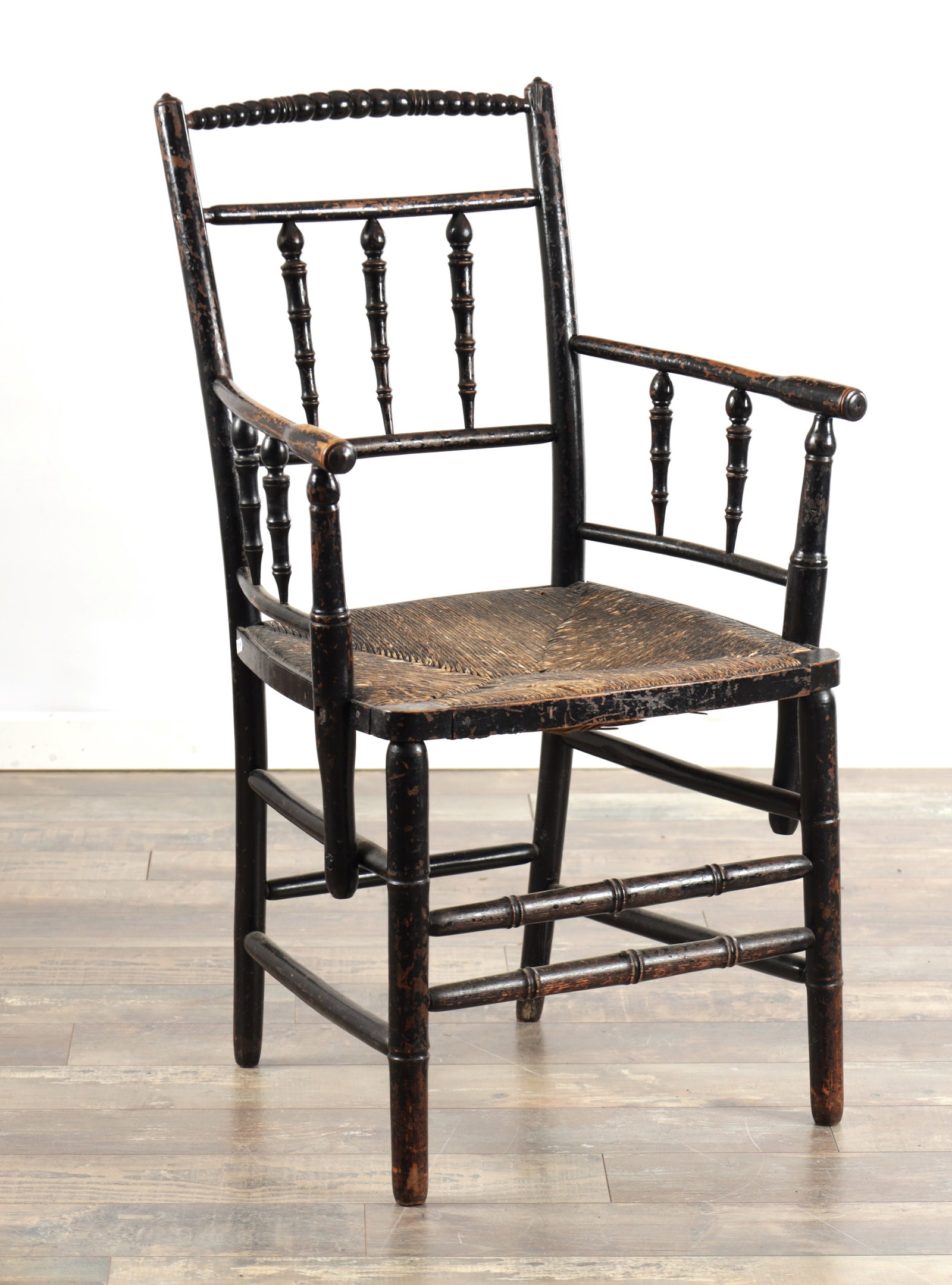 A LATE 19TH CENTURY ENGLISH ARTS AND CRAFTS EBONISED BEECH SUSSEX ARMCHAIR WITH RUSH SEAT: A LATE 19TH CENTURY ENGLISH ARTS AND CRAFTS EBONISED BEECH SUSSEX ARMCHAIR WITH RUSH SEAT having a bobbin turned top rail over three baluster spindles, downswept arms with spindled supports, a square