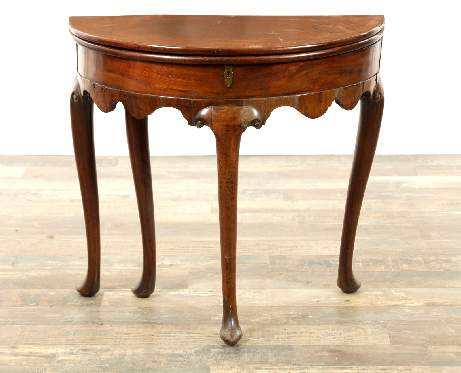 A GEORGE II MAHOGANY DEMI LUNE TEA TABLE: A GEORGE II MAHOGANY DEMI LUNE TEA TABLE with hinged fold-over top revealing a well having a deep frieze with shaped apron raised on cabriole legs with pointed feet. (82cm wide 40cm deep 74cm high )