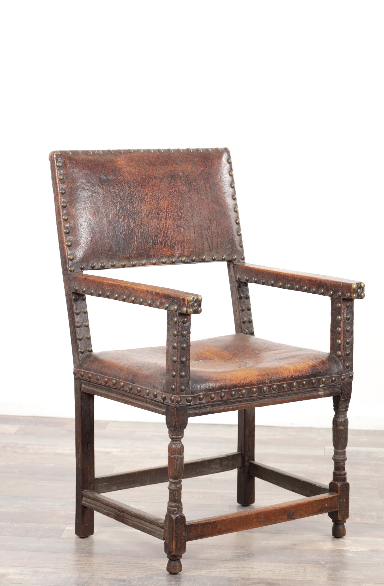 A 17TH CENTURY OAK FRAMED LEATHER UPHOLSTERED ARMCHAIR: A 17TH CENTURY OAK FRAMED LEATHER UPHOLSTERED ARMCHAIR with brass studwork, the rectangular padded back and seat within a plain frame, open arms with leather pads, raised on block and ring turned fron