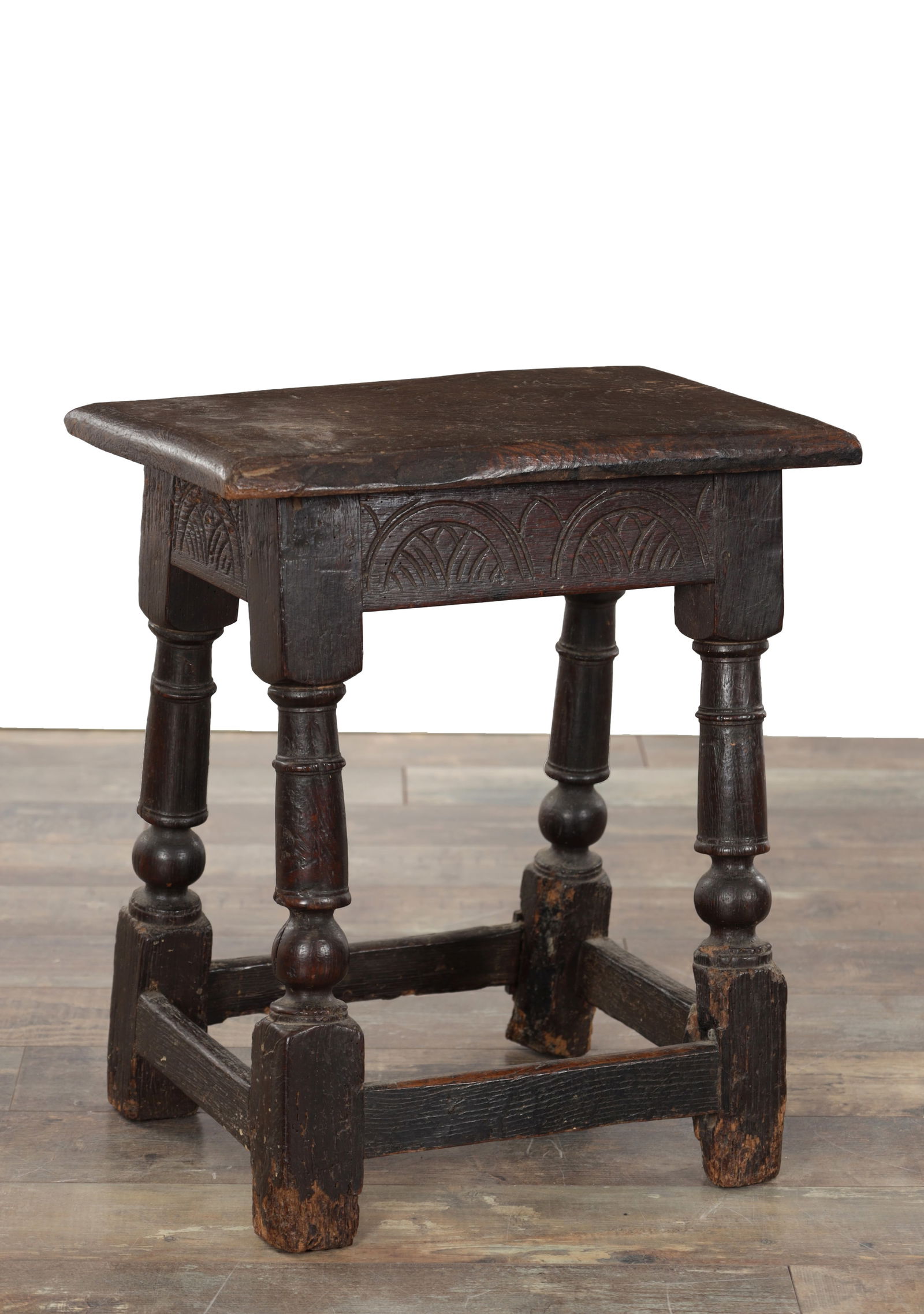 A 17TH CENTURY OAK JOINT STOOL: A 17TH CENTURY OAK JOINT STOOL the rectangular plank top above a carved frieze with repeating arch and fan motifs, raised on four turned legs united by stretchers. (44cm 27cm deep 50cm high )